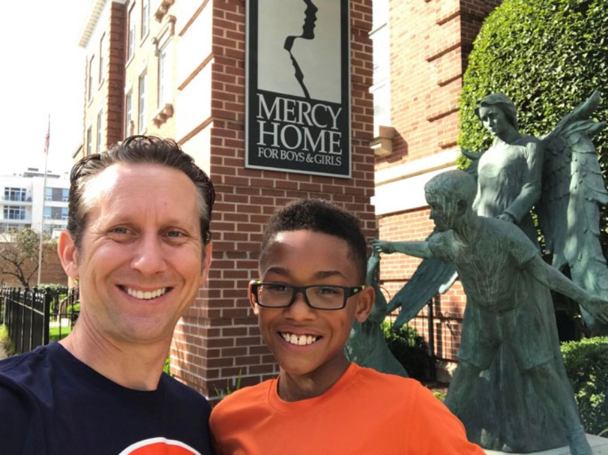 Scott e seu filho adotivo Demetrius sorriem em frente ao orfanato “Mercy Home” - exatamente onde o avô de Scott um dia encontrou um novo lar. Scott e seu filho adotivo Demetrius sorriem em frente ao orfanato “Mercy Home” - exatamente onde o avô de Scott um dia encontrou um novo lar.