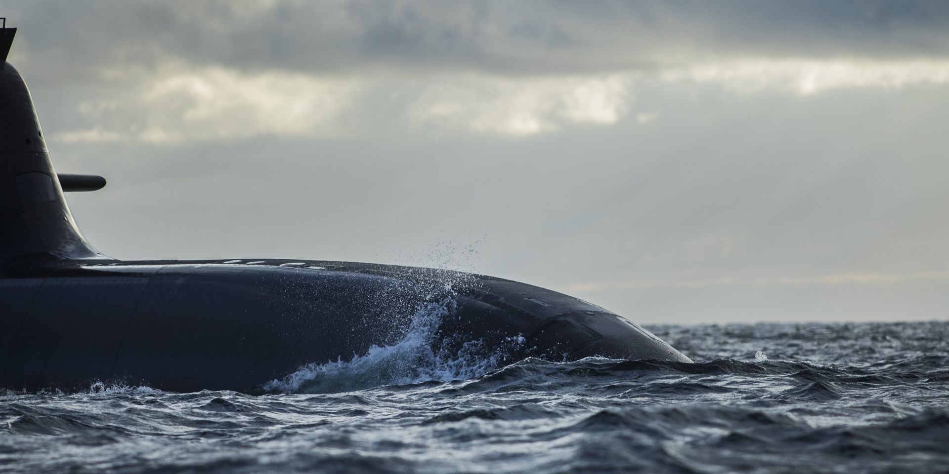 Ein dunkles U-Boot fährt bei bewölktem Himmel durch ein aufgewühltes Meer.