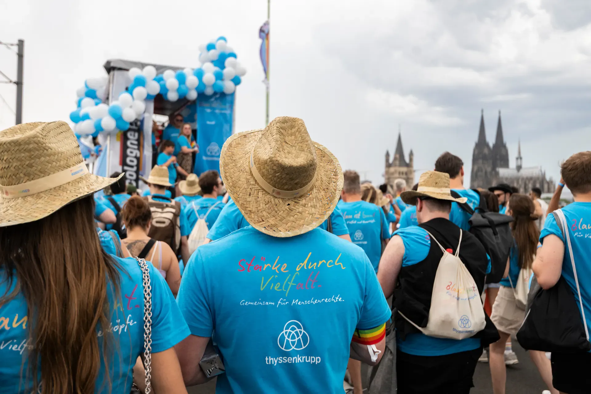 Teilnehmer der Kölner Pride-Parade in blauen thyssenkrupp-T-Shirts mit dem Motto „Stärke durch Vielfalt“ vor dem Kölner Dom.