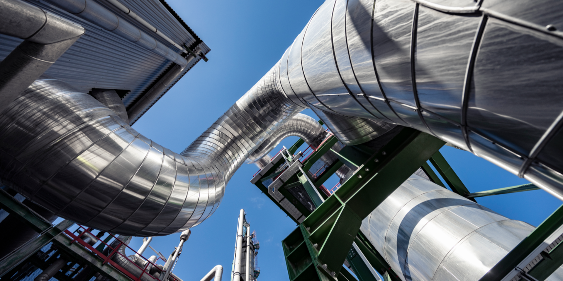Metallische Rohrleitungen und Stahlkonstruktionen einer Chemieanlage vor blauem Himmel.