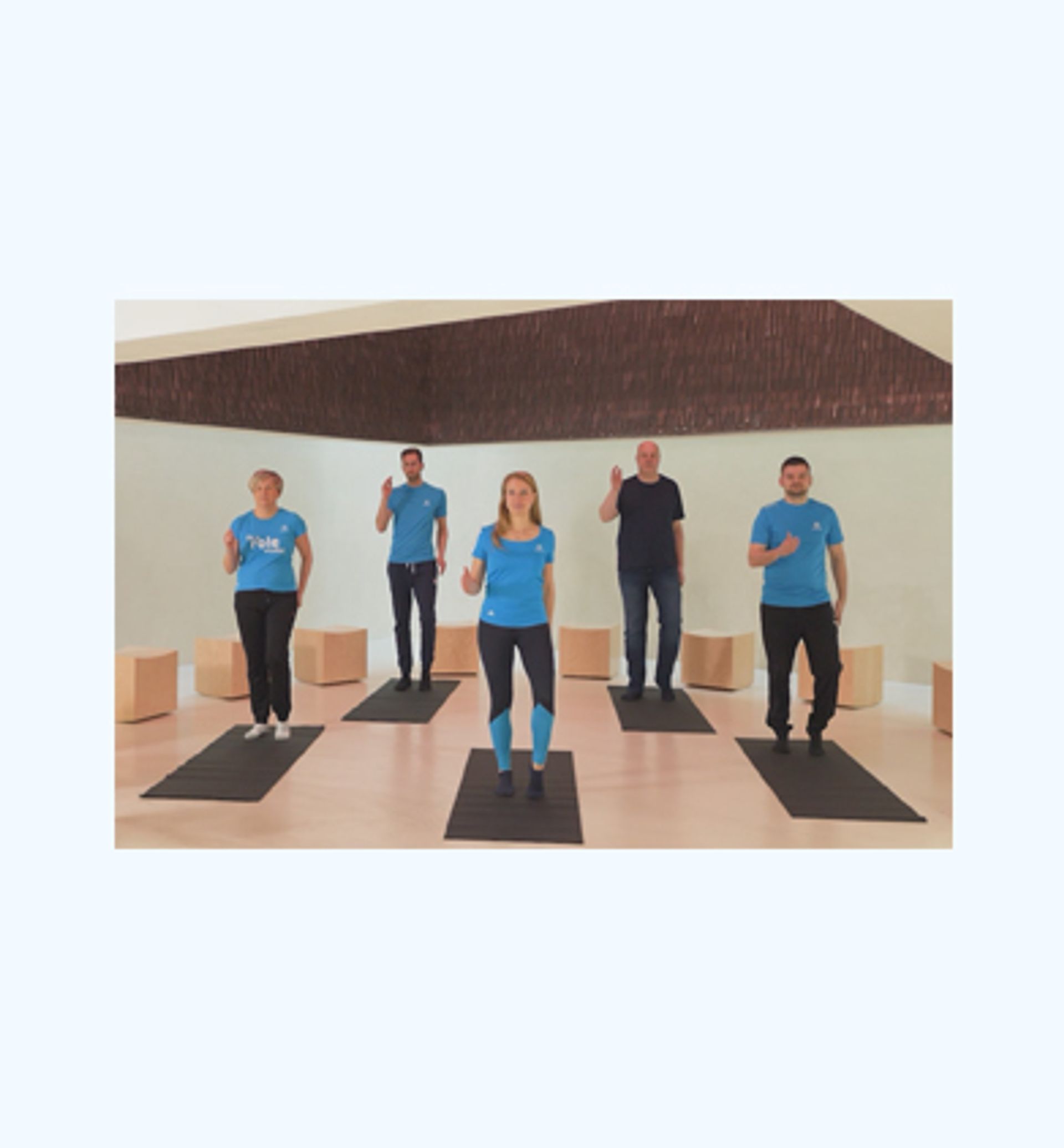 Fünf Beschäftigte in Sportkleidung machen gemeinsam Übungen auf Gymnastikmatten in einem hellen Raum.