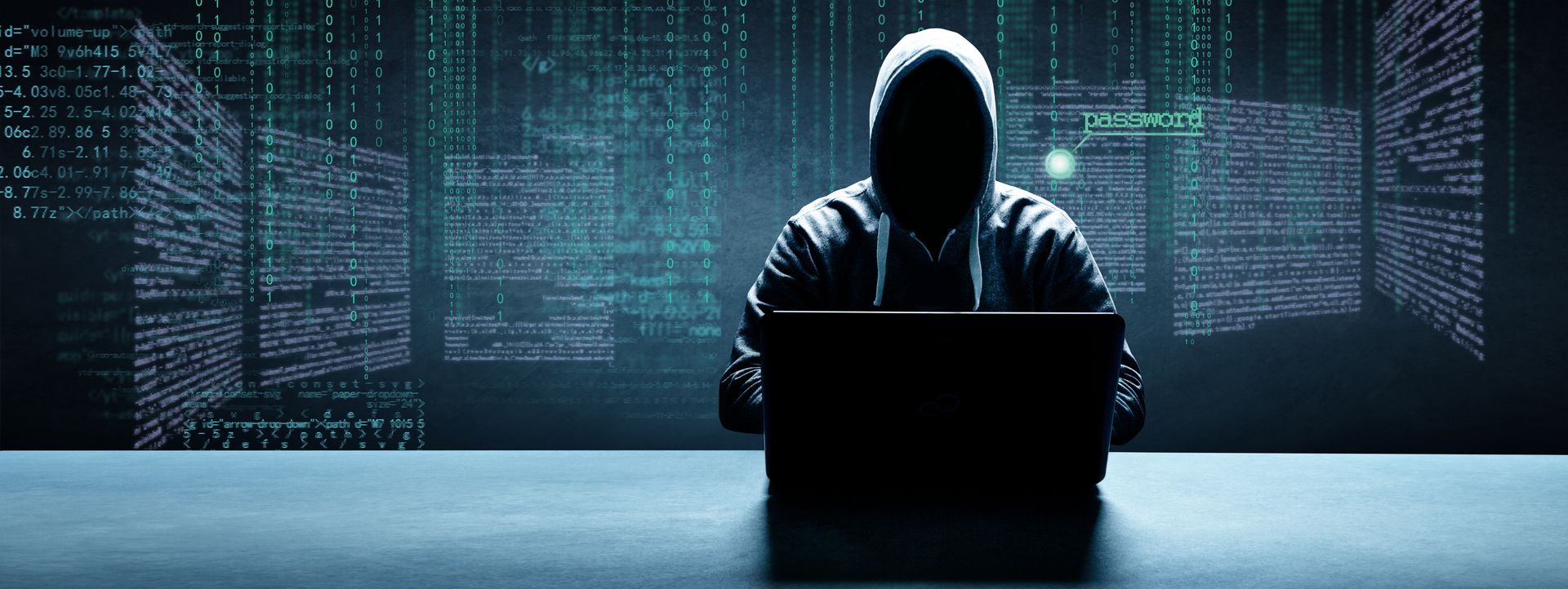 Person in dunklem Hoodie sitzt vor geöffnetem Laptop, im Hintergrund Datensätze