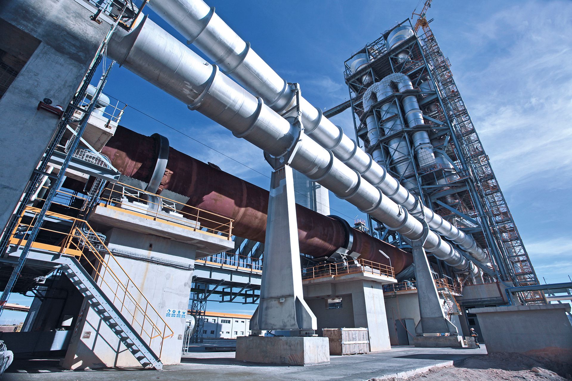 Große Industrieanlage mit Rohrleitungen und Stahlgerüst vor blauem Himmel.