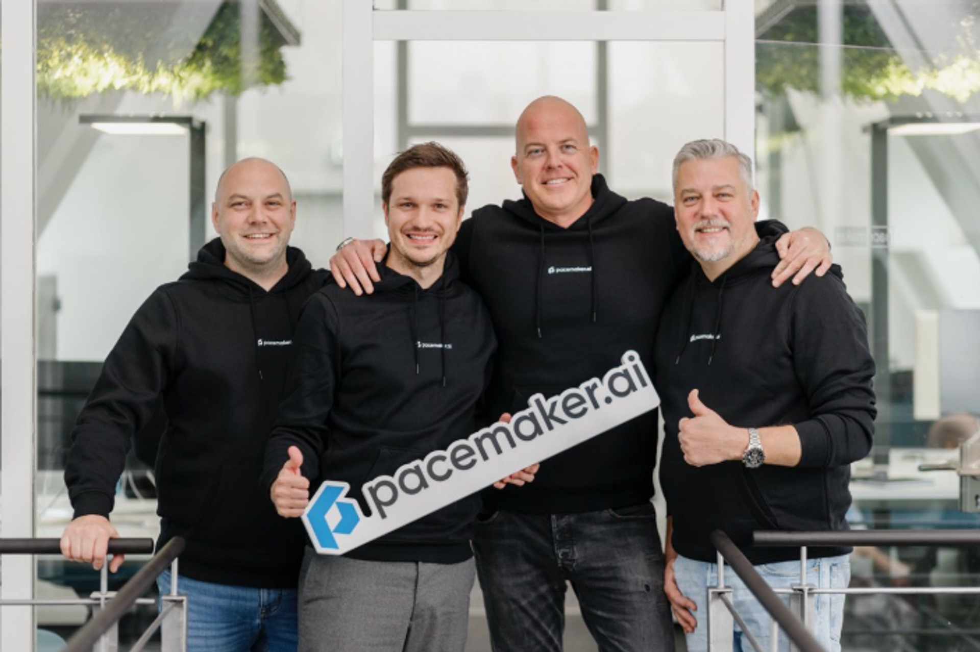 Vier Mitarbeitende von pacemaker.ai stehen gemeinsam in einem modernen Büro und halten ein pacemaker.ai Logo-Schild in die Kamera.