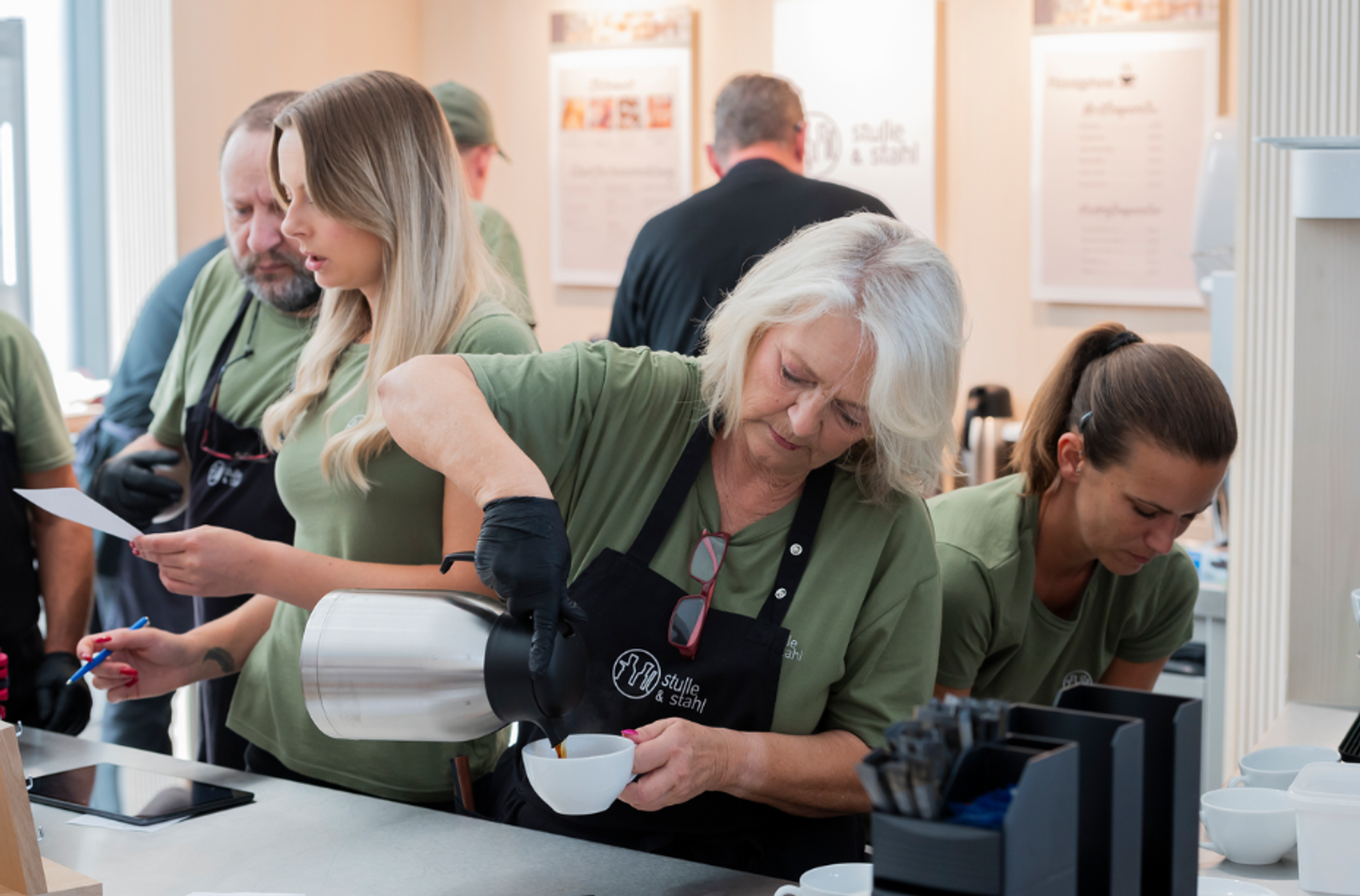 Das Team im Café; Eine Mitarbeiterin schüttet Kaffee in eine Tasse 
