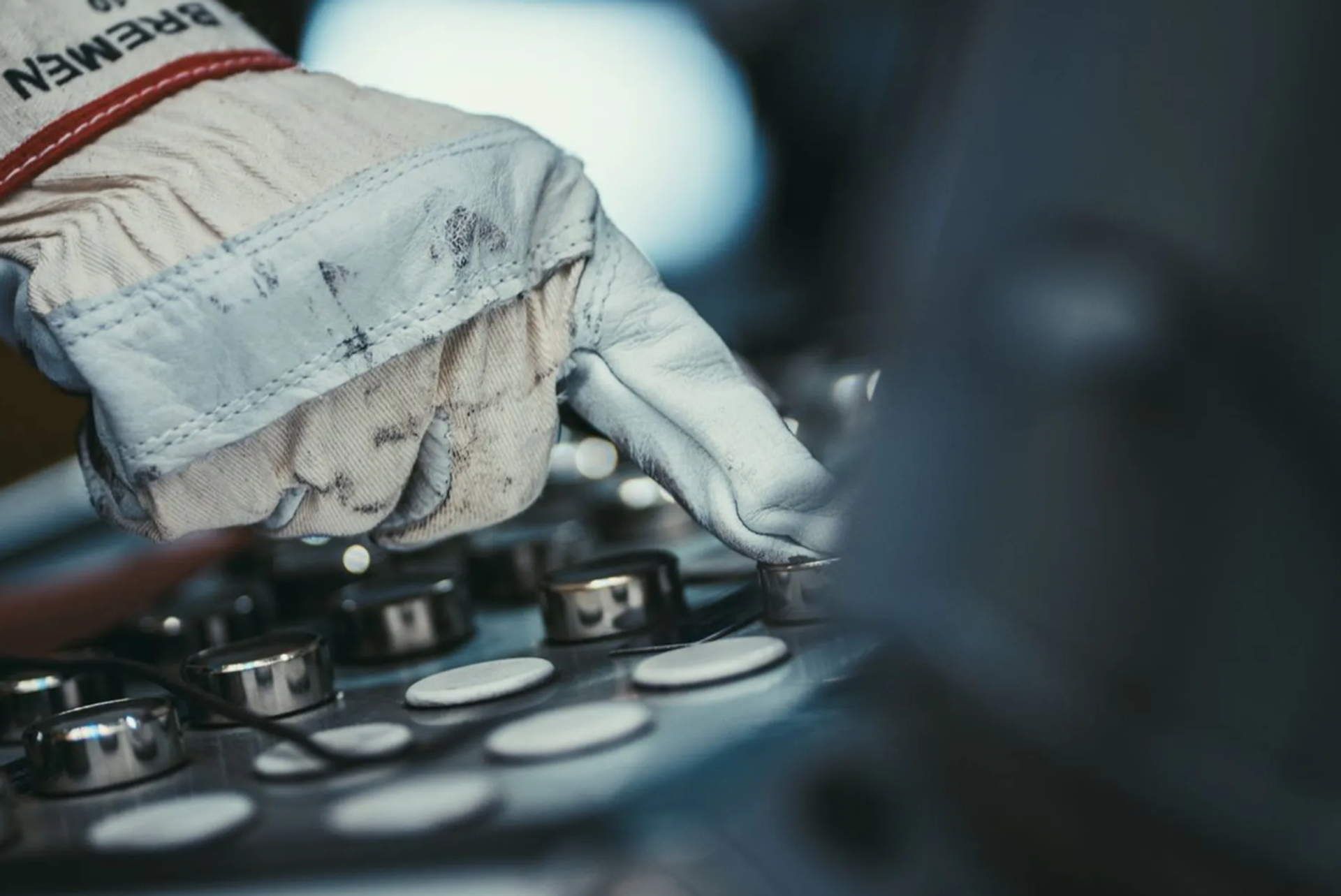 Close-up of a hand wearing a work glove pressing a button on an industrial control panel.