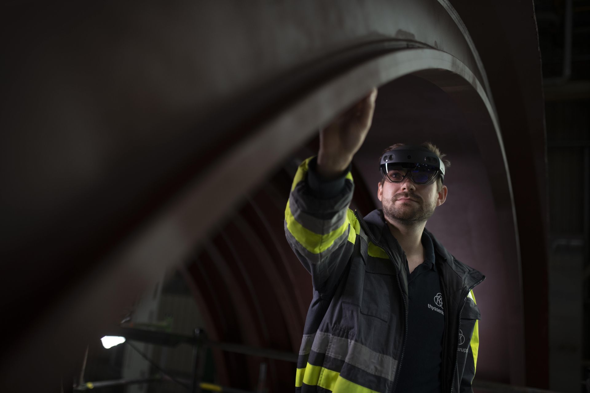 An employee wearing a helmet and protective gear is inspecting a metal structure inside a ship.