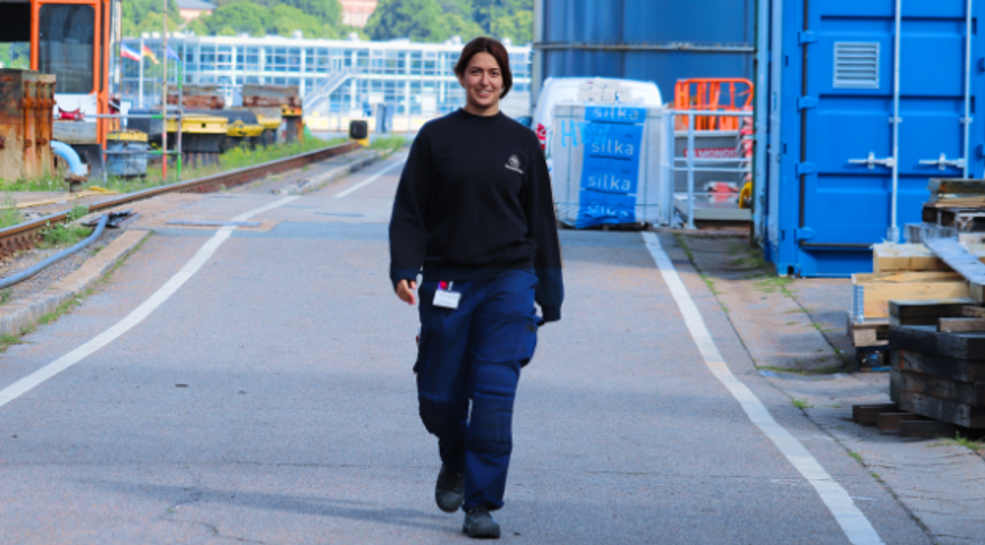female read person in work clothes, walking across the outdoor area of a tkMS location
