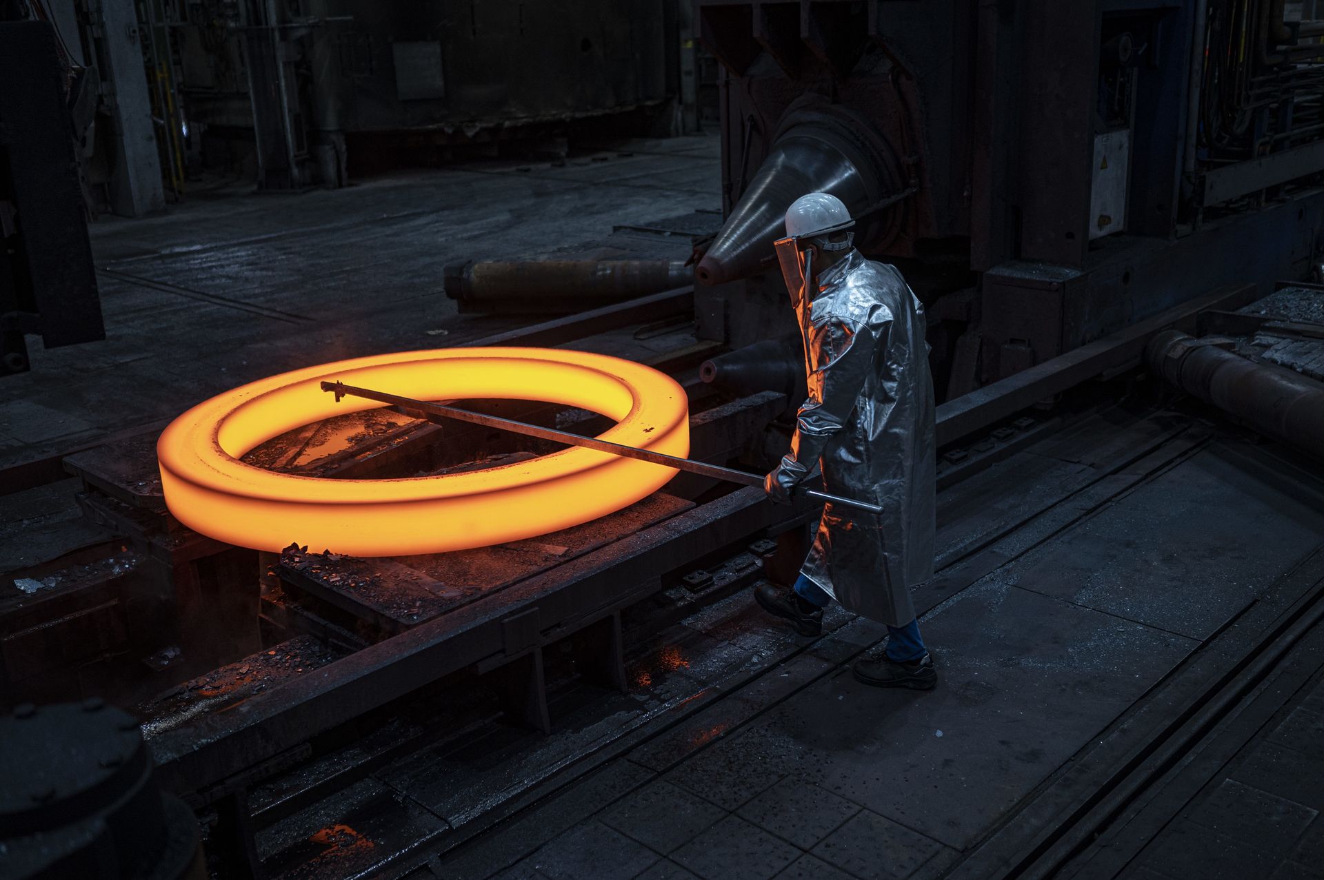 Ein thyssenkrupp Mitarbeiter bearbeitet einen glühenden, nahtlos gewalzten Ring in einer Fertigungsanlage