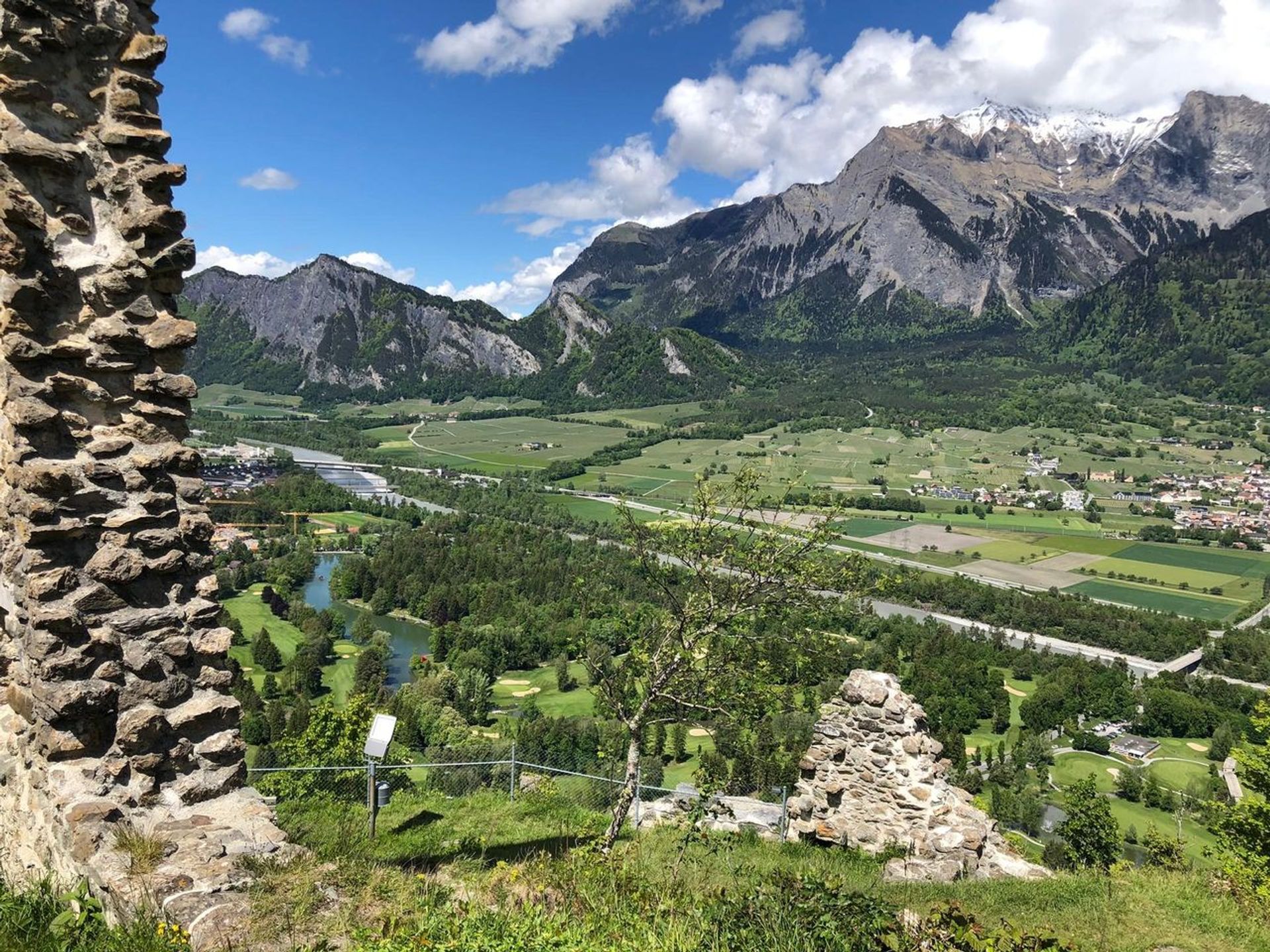 Ausblick auf eine grüne Landschaft, bewachsene Felder und Berge im Hintergrund
