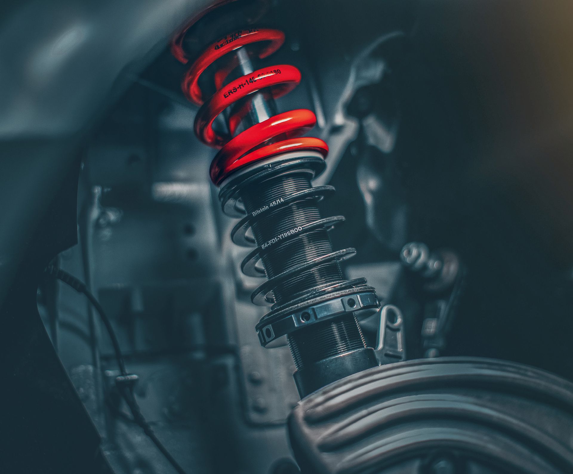 Nahaufnahme eines eingebauten BILSTEIN Gewindefahrwerks mit schwarzem Dämpferrohr, roter Feder und Einstellringen im Radhaus eines Fahrzeugs.