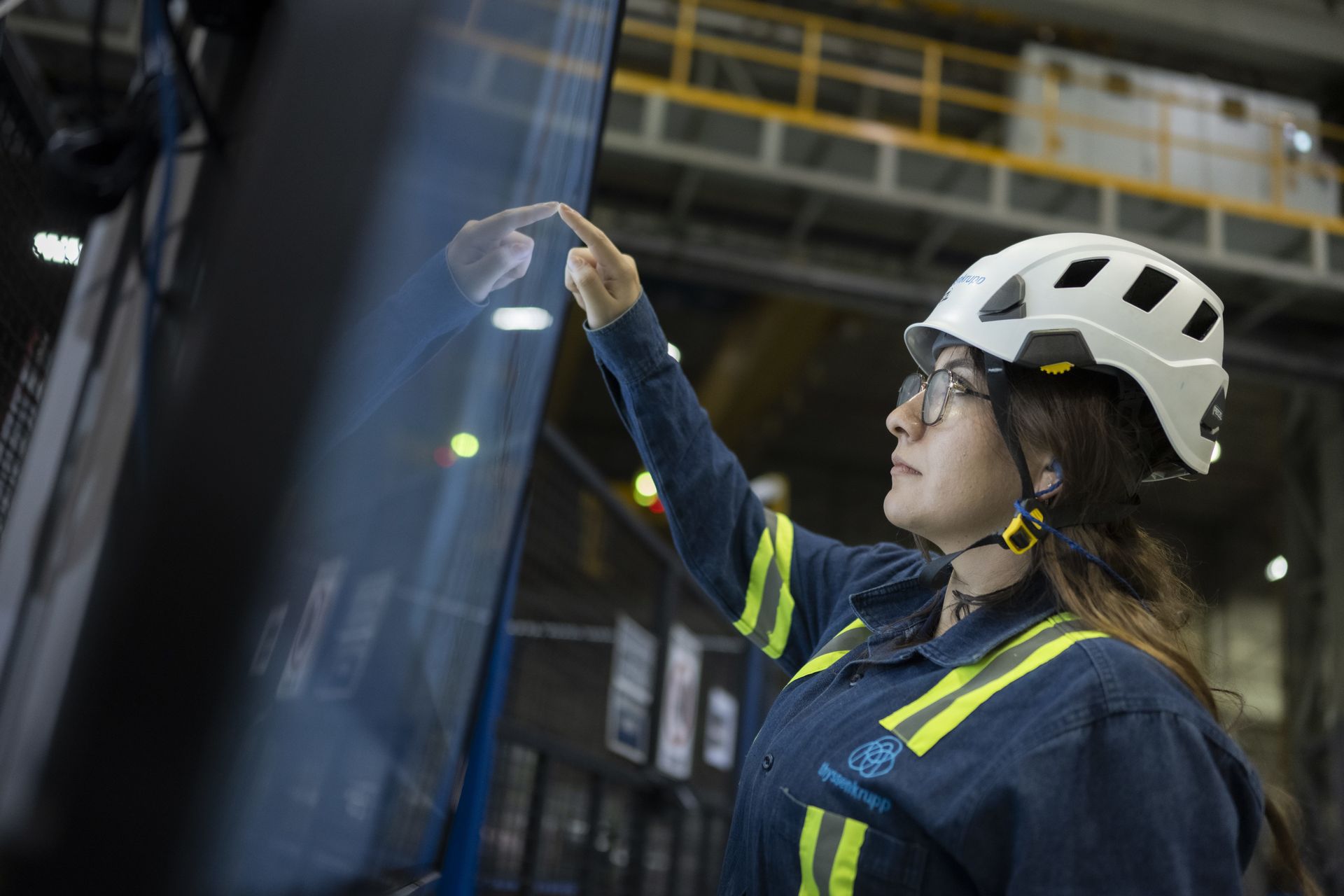 A thyssenkrupp employee monitors production data on a digital control panel in an industrial manufacturing environment.