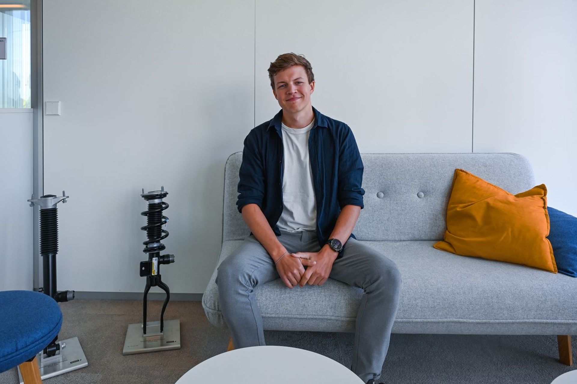 Felix Ewering von thyssenkrupp Bilstein steht vor einem Regal mit Fahrzeugmodellen, technischen Bauteilen und gerahmten Projektmotiven.