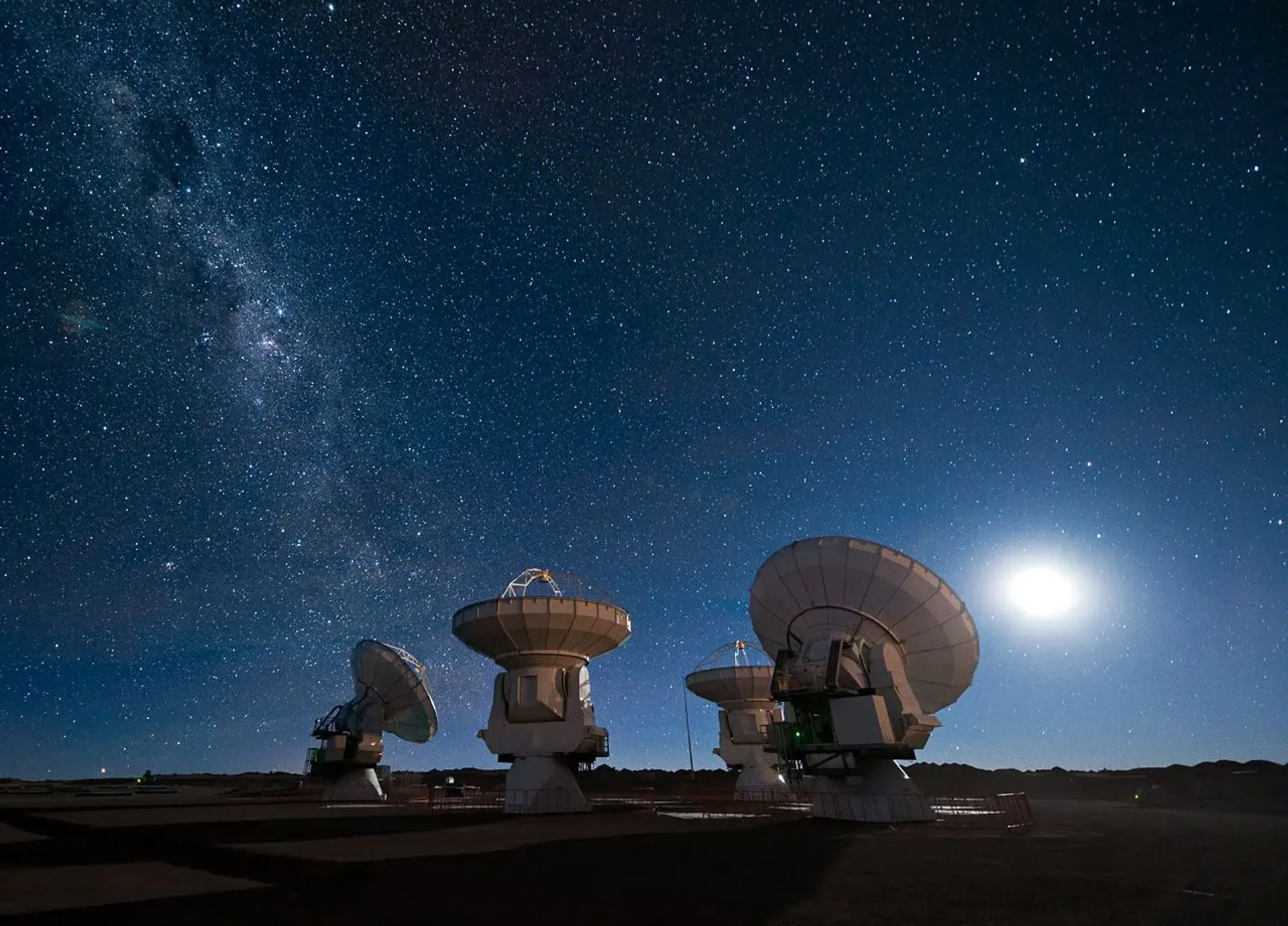 Mehrere Antennen des Radioteleskops ALMA auf dem Chajnantor-Plateau in der chilenischen Atacamawüste unter einem klaren Sternenhimmel.