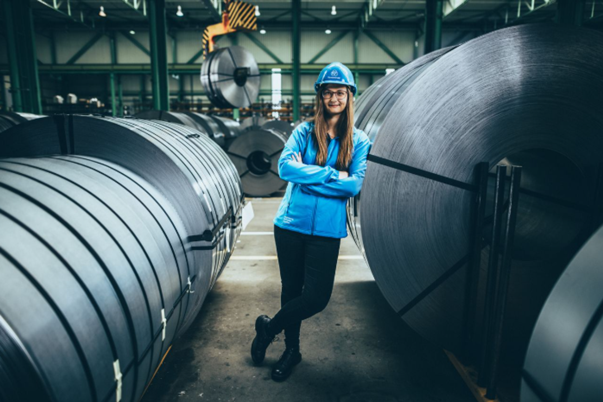 Mitarbeiterin von thyssenkrupp zwischen Stahlcoils in einer Produktionshalle der Stahlverarbeitung.
