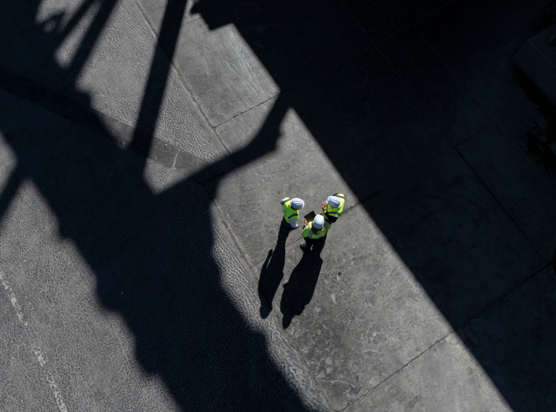 Drei thyssenkrupp Mitarbeitende mit Schutzkleidung unterhalten sich im Schatten einer Industrieanlage.