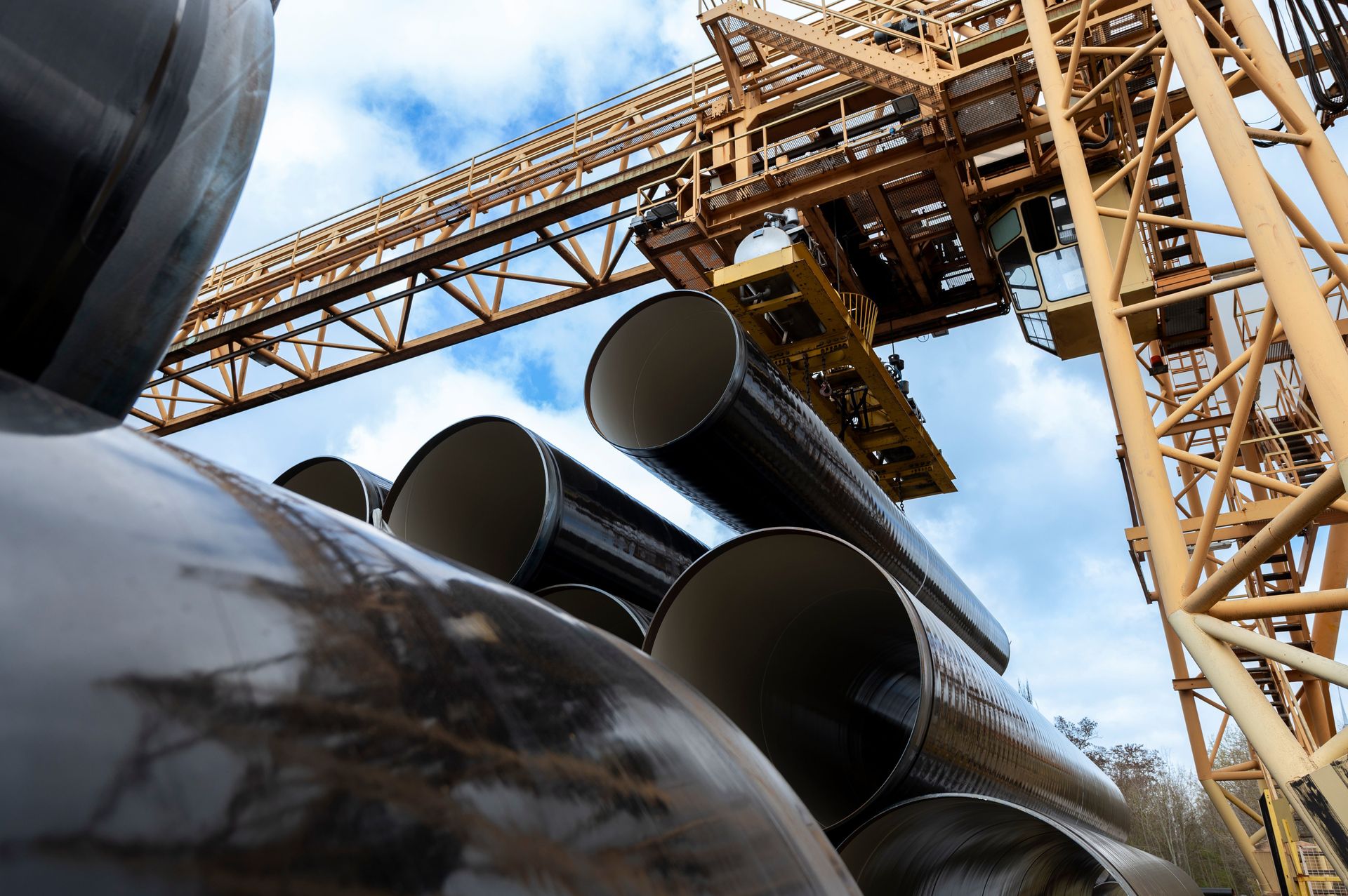Large steel pipes are moved by a crane at a storage facility.