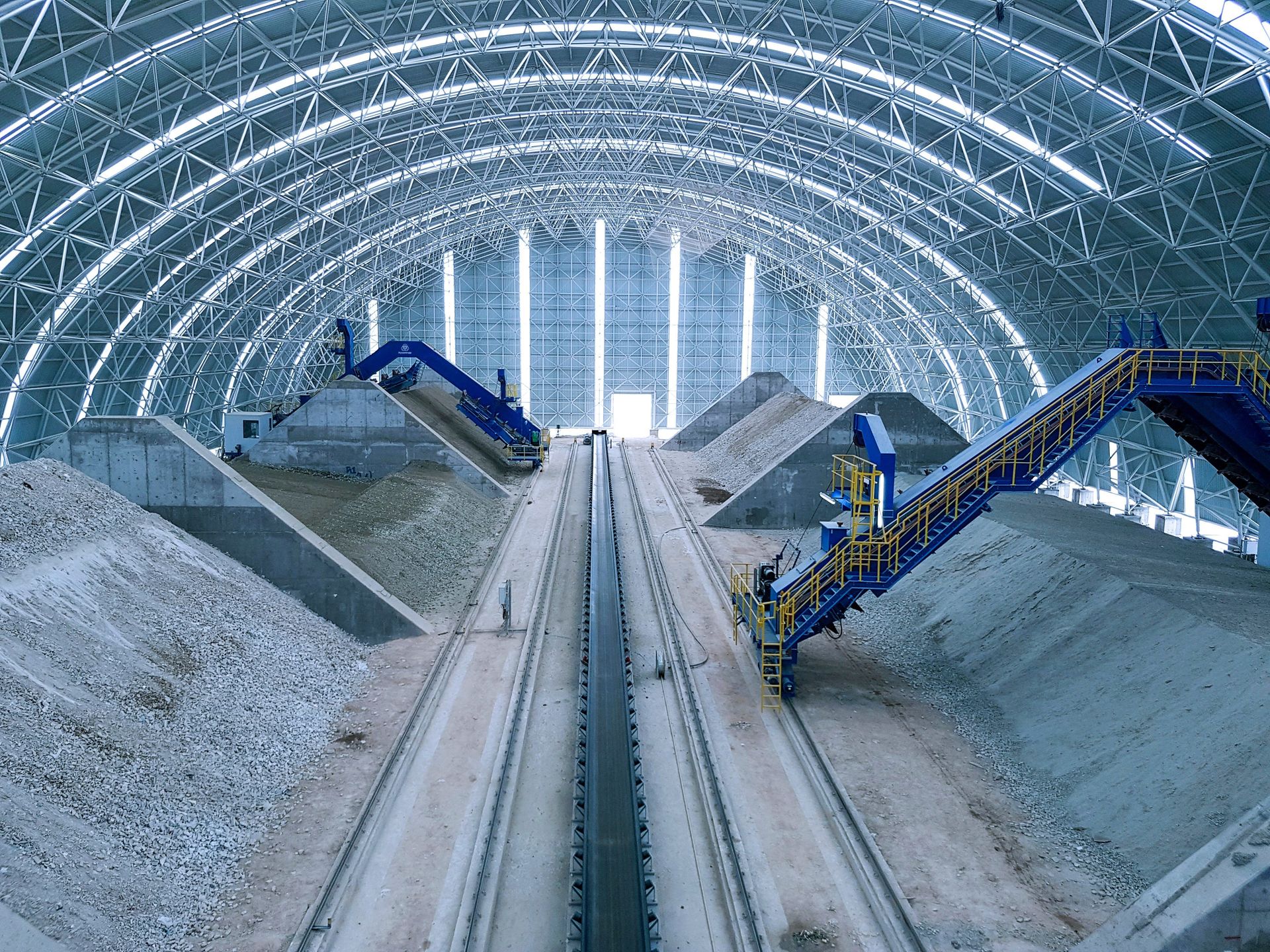 nclosed storage hall at a cement plant with conveyor systems and bulk material stockpiles for the storage and transport of raw materials used in cement production.