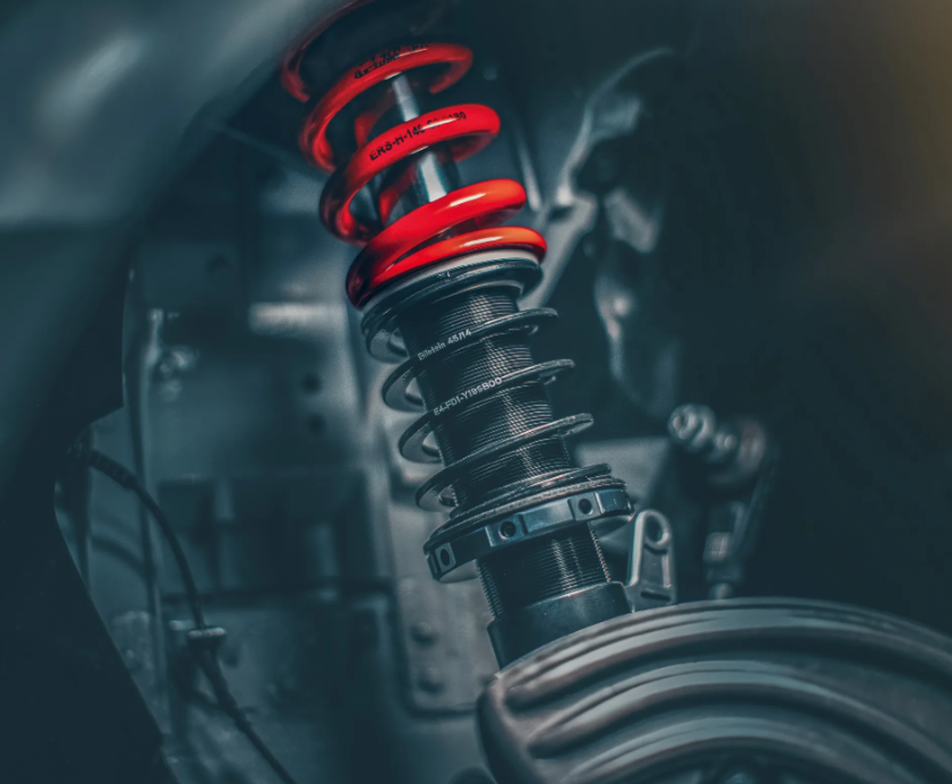 Nahaufnahme eines eingebauten BILSTEIN Gewindefahrwerks mit schwarzem Dämpferrohr, roter Feder und Einstellringen im Radhaus eines Fahrzeugs.