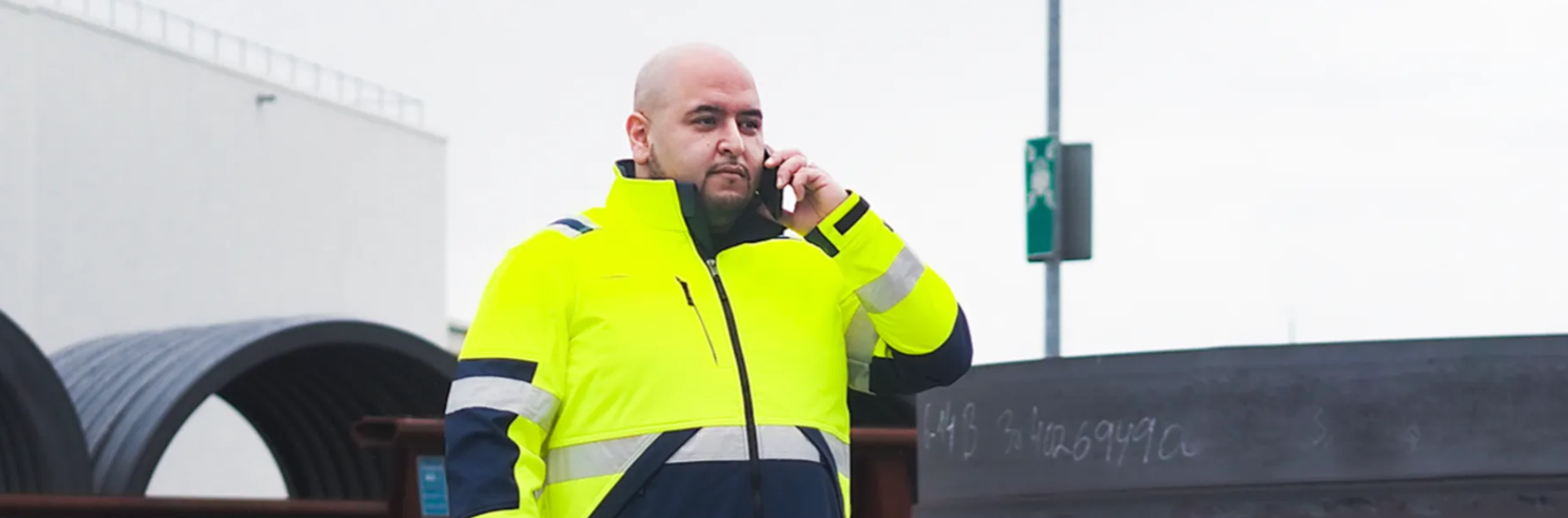 männlich gelesene Person in gelber Schutzjacke, hält ein Handy am Ohr