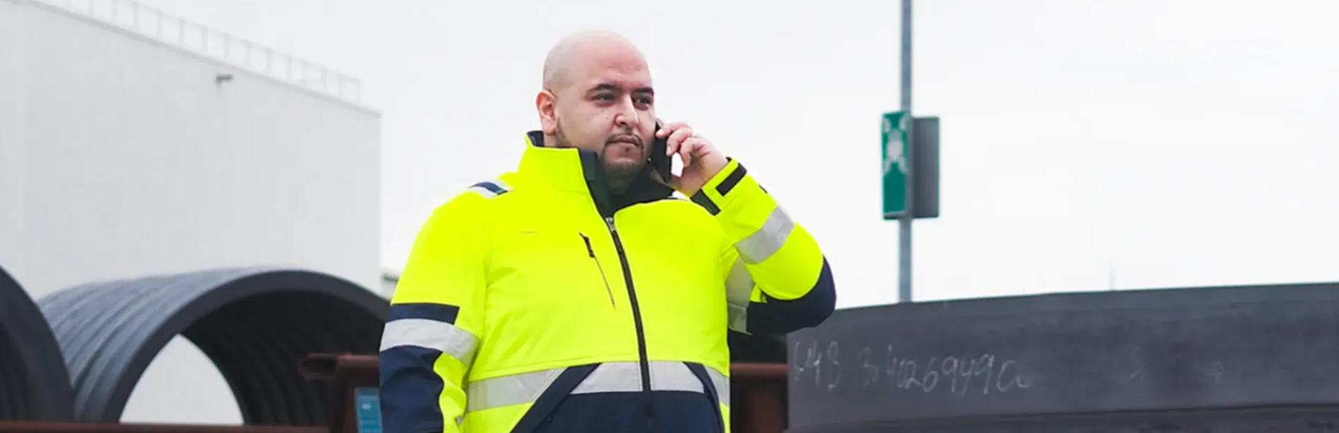 männlich gelesene Person in gelber Schutzjacke, hält ein Handy am Ohr