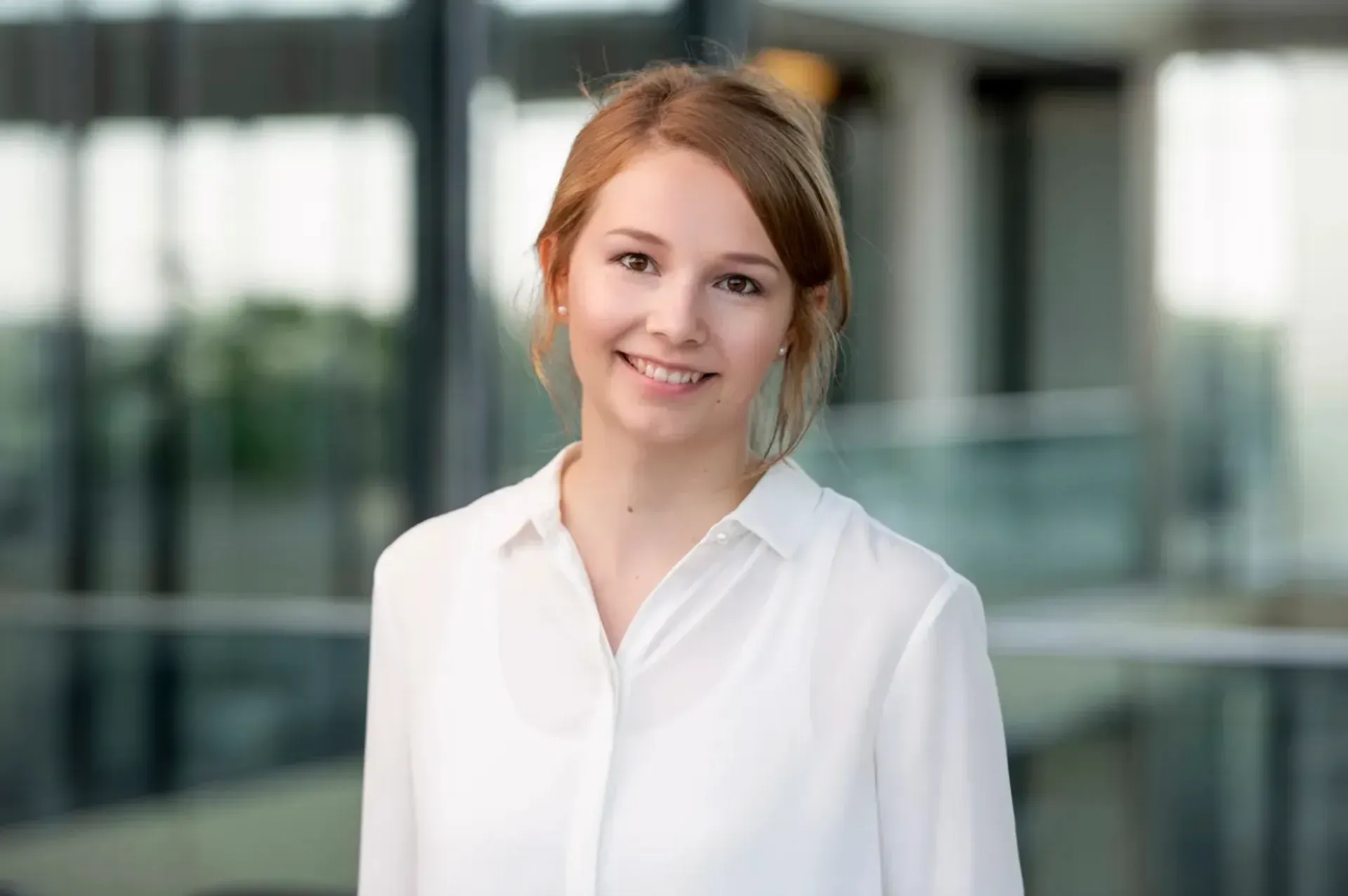 A smiling woman in a white shirt is standing in a modern office building.