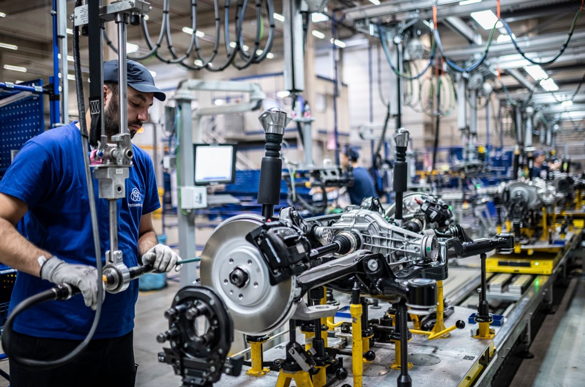 Ein Mitarbeiter von thyssenkrupp arbeitet in einer modernen Produktionshalle an der Montage eines Fahrwerksmoduls. Die Aufnahme zeigt industrielle Fertigung, Engineering-Kompetenz und innovative Technologien für die Automobilindustrie.