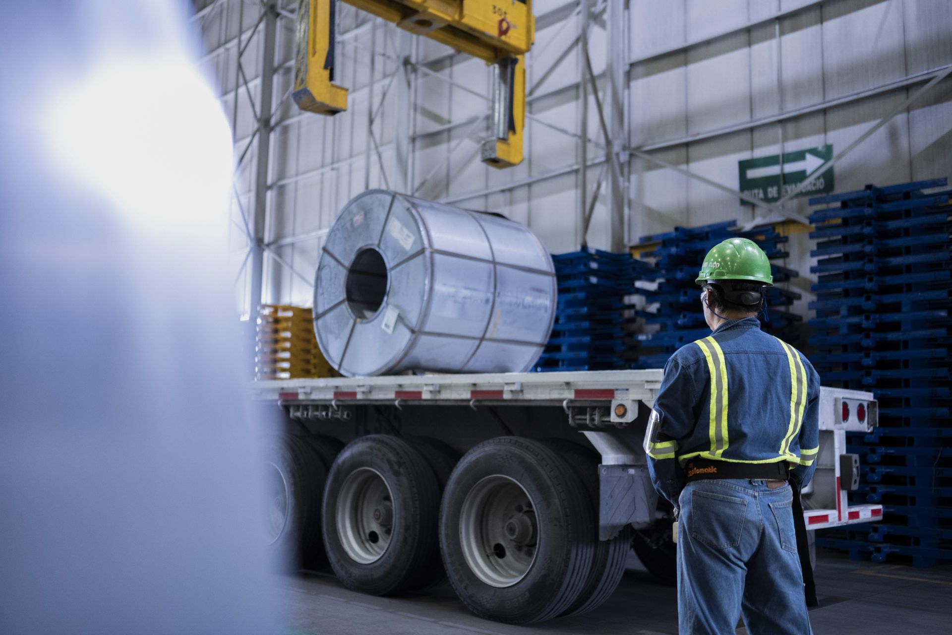 thyssenkrupp Mitarbeiter mit Schutzkleidung neben einem Lastwagen, der ein großes Stahlcoil transportiert.