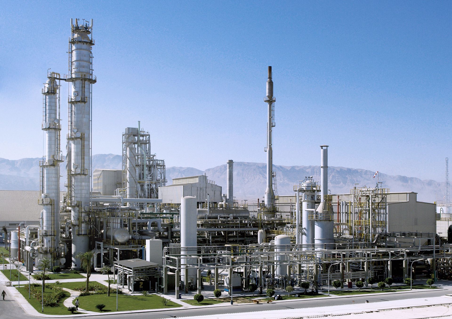 thyssenkrupp Uhde industrial plant with pipelines, reactors, and tall process towers against a mountainous landscape.