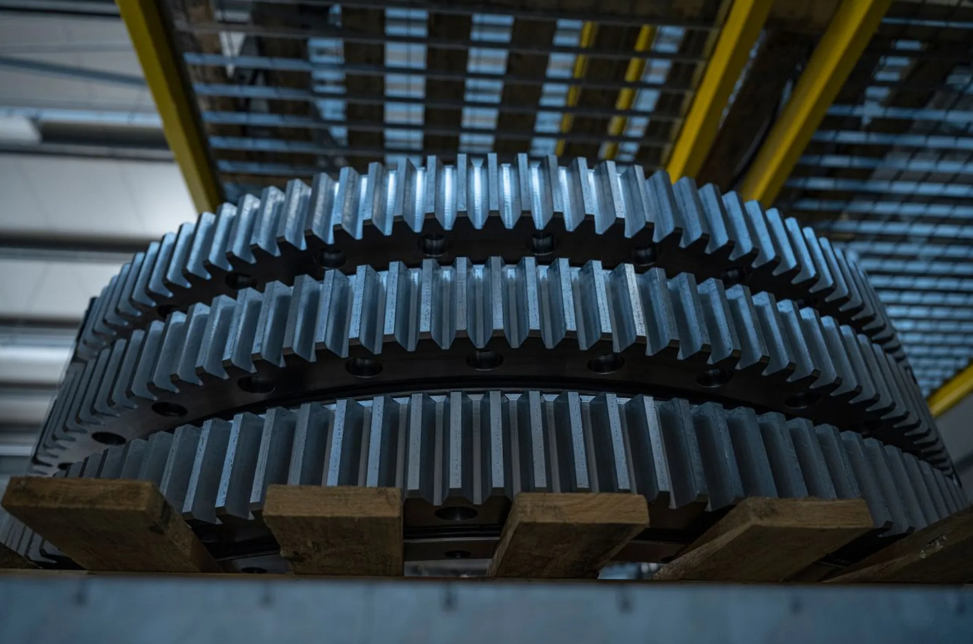 Nahaufnahme mehrerer großer verzahnter Metallringe, die übereinandergestapelt auf einer Palette in einer Produktionshalle liegen.
