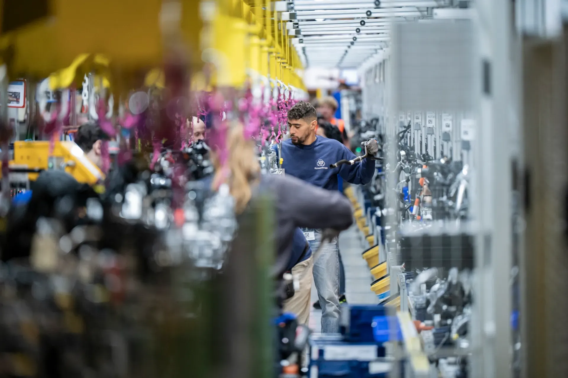 Mitarbeitende von thyssenkrupp montieren Fahrzeugkomponenten an einer industriellen Fertigungslinie.
