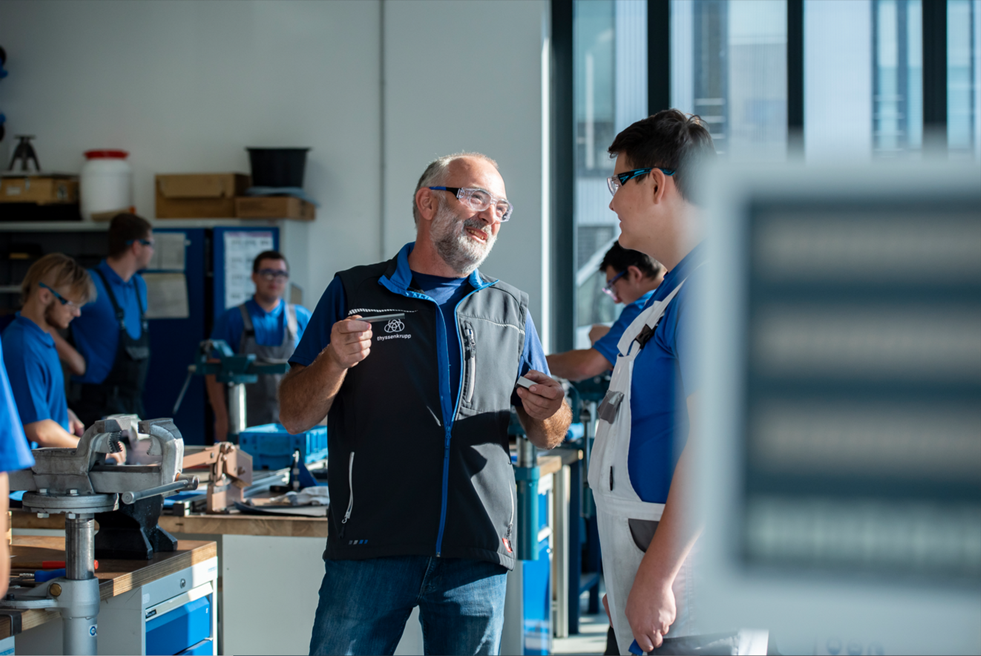 Ein Ausbilder erklärt einem Auszubildenden Arbeitsschritte in einer technischen Werkstatt bei thyssenkrupp