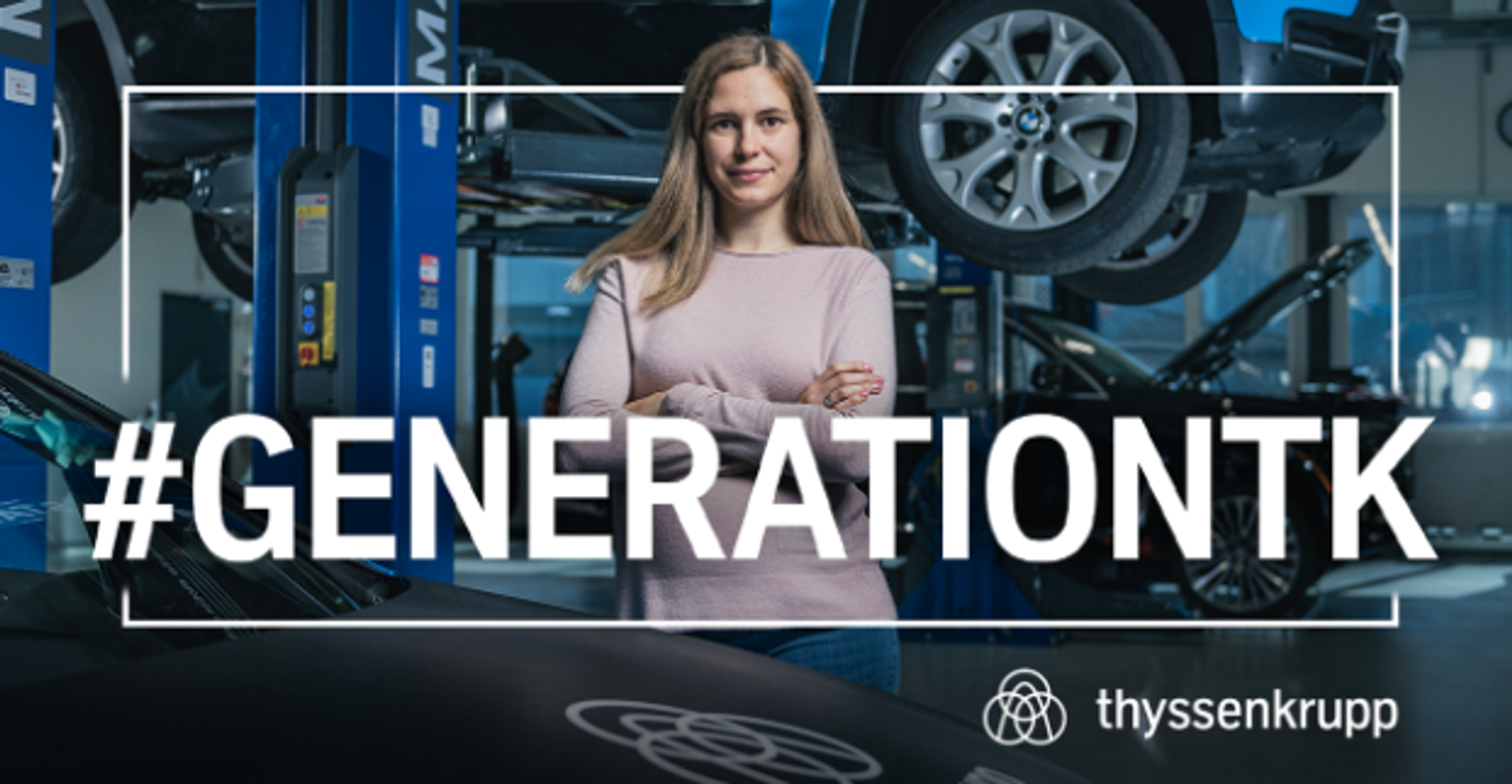 weiblich Gelesene Person mit langen blonden Harren, rosa Oberteil, mit verschränkten Armen in eine Autohalle stehend