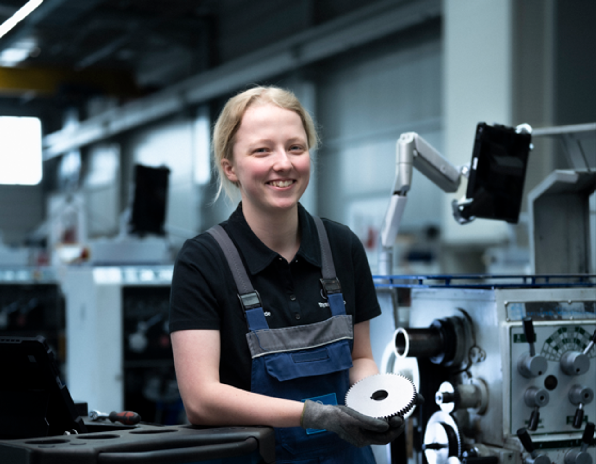 A thyssenkrupp apprentice smiles while holding a precision-engineered component in a modern manufacturing environment.