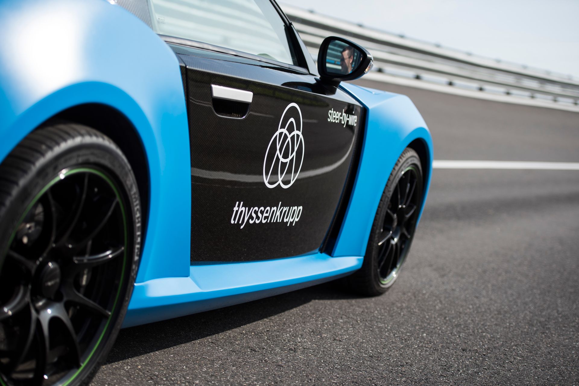 Seitliche Nahaufnahme eines blau-schwarzen thyssenkrupp Testfahrzeugs auf einer Teststrecke.