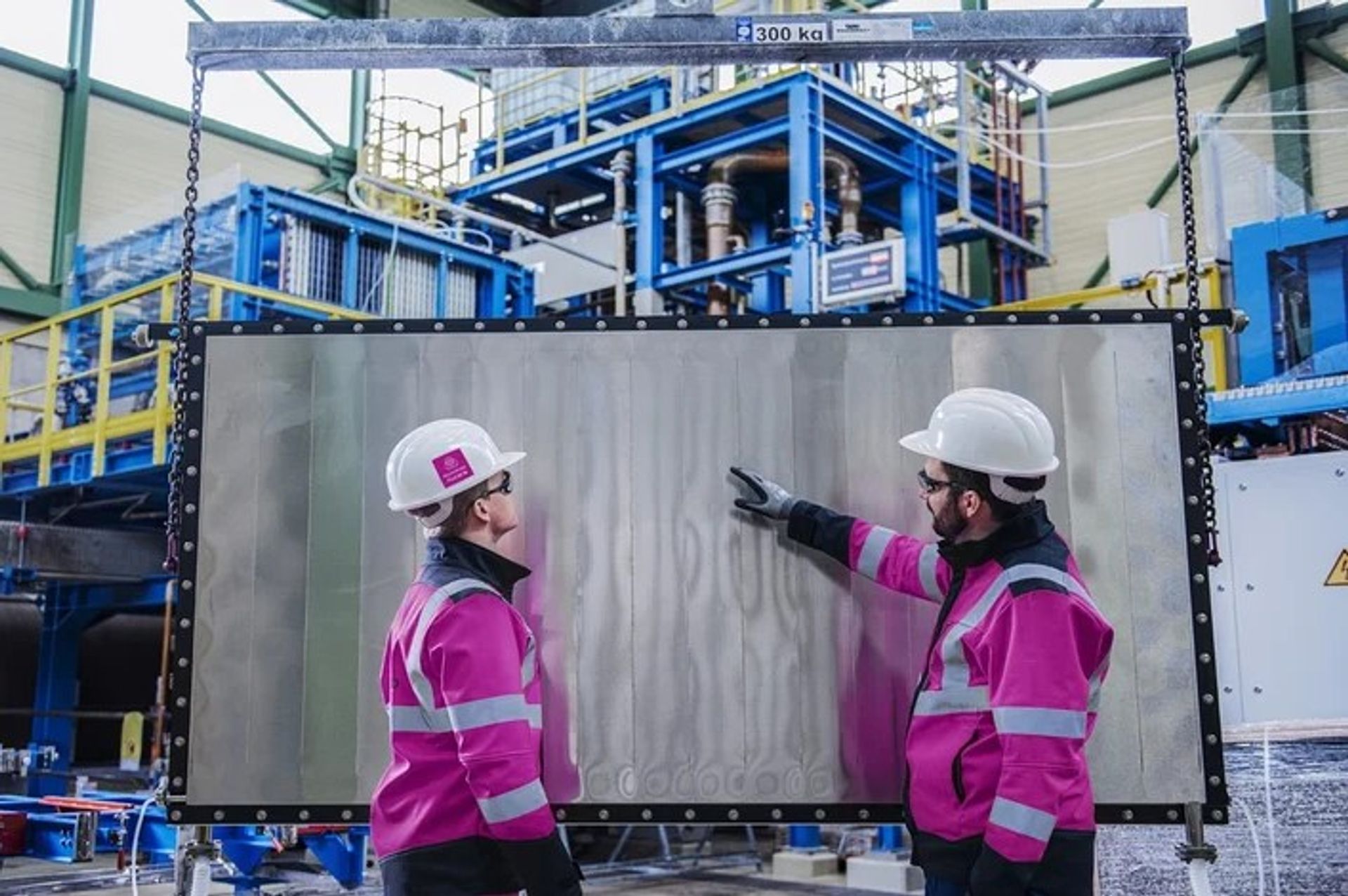 Two employees standing in front of a water electrolysis module from thyssenkrupp nucera. 