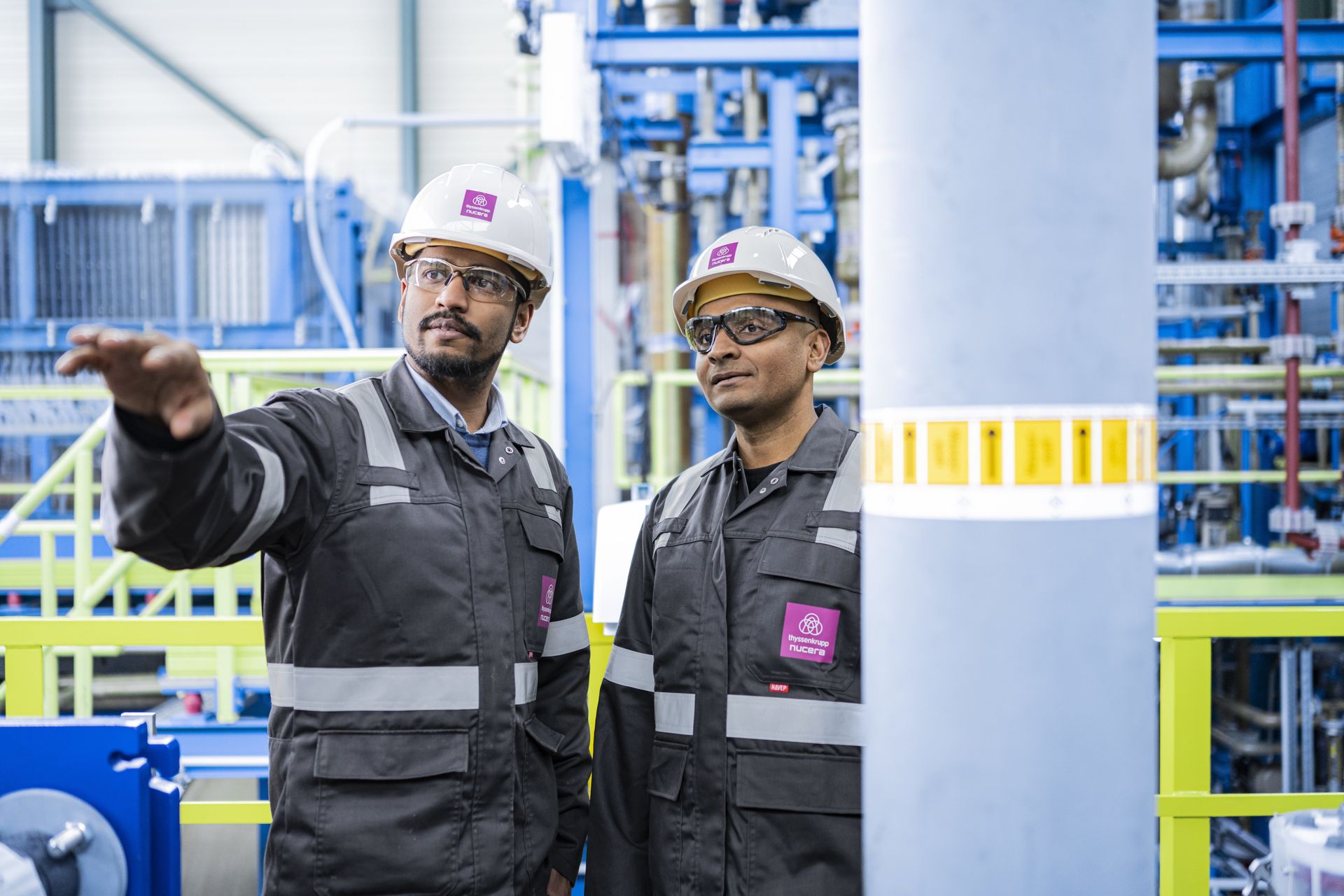 Zwei Mitarbeitende von thyssenkrupp nucera besprechen eine Industrieanlage während einer technischen Inspektion.
