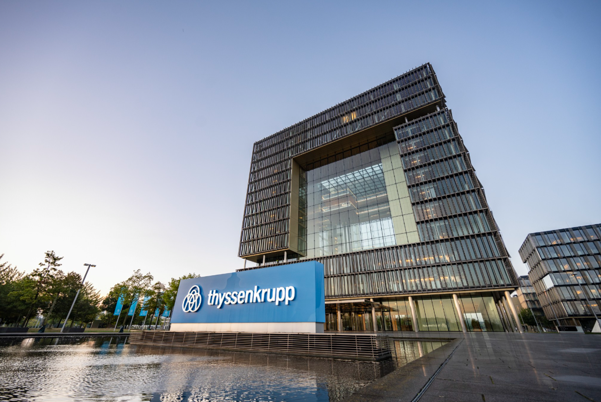 Moderne Glas- und Stahlarchitektur der thyssenkrupp Unternehmenszentrale in Essen mit großem Firmenlogo vor dem Gebäude.