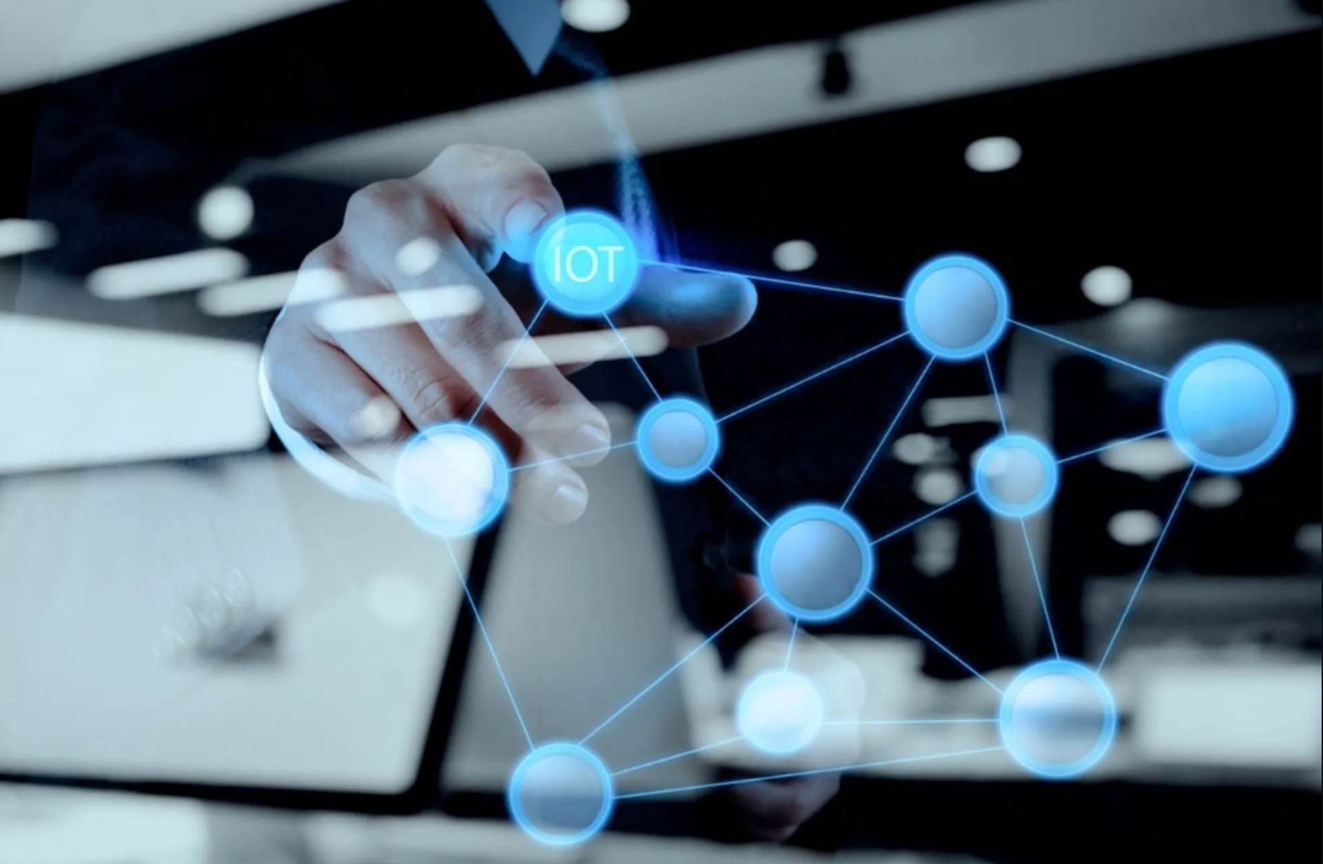 Close-up of a hand interacting with a digital IoT network visualization featuring interconnected blue nodes.
