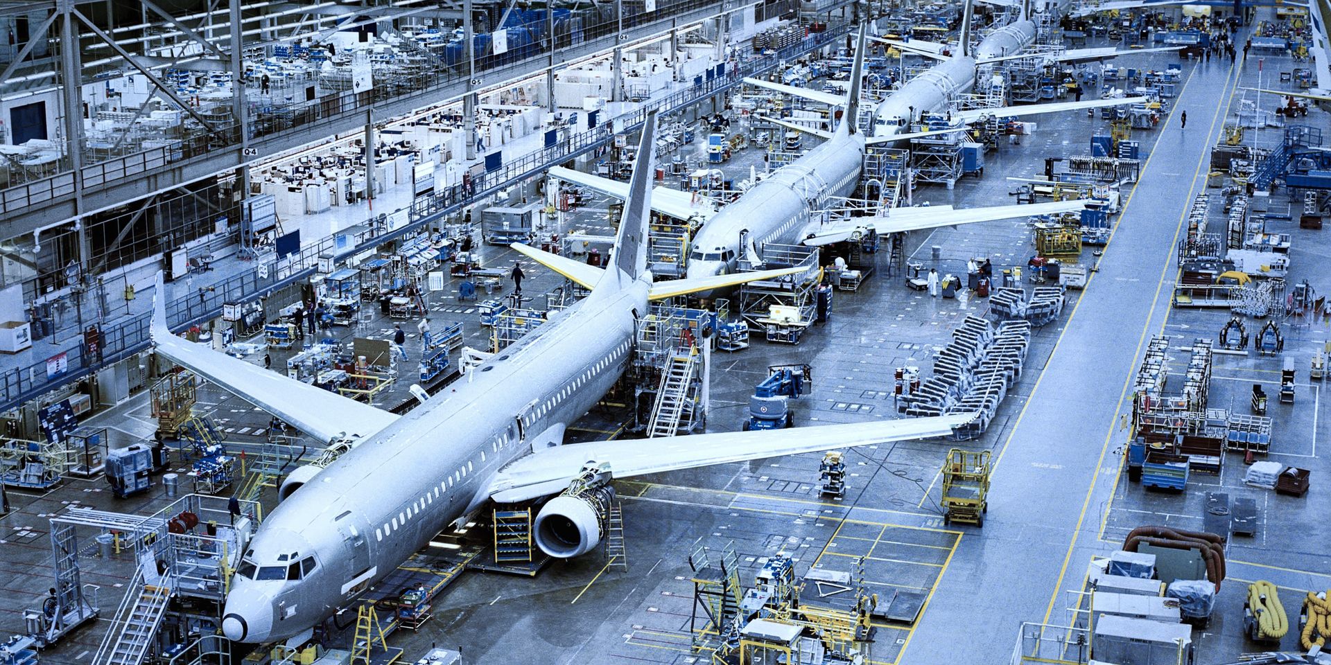 Mehrere Verkehrsflugzeuge stehen an verschiedenen Fertigungsstationen in einer großen Montagehalle.