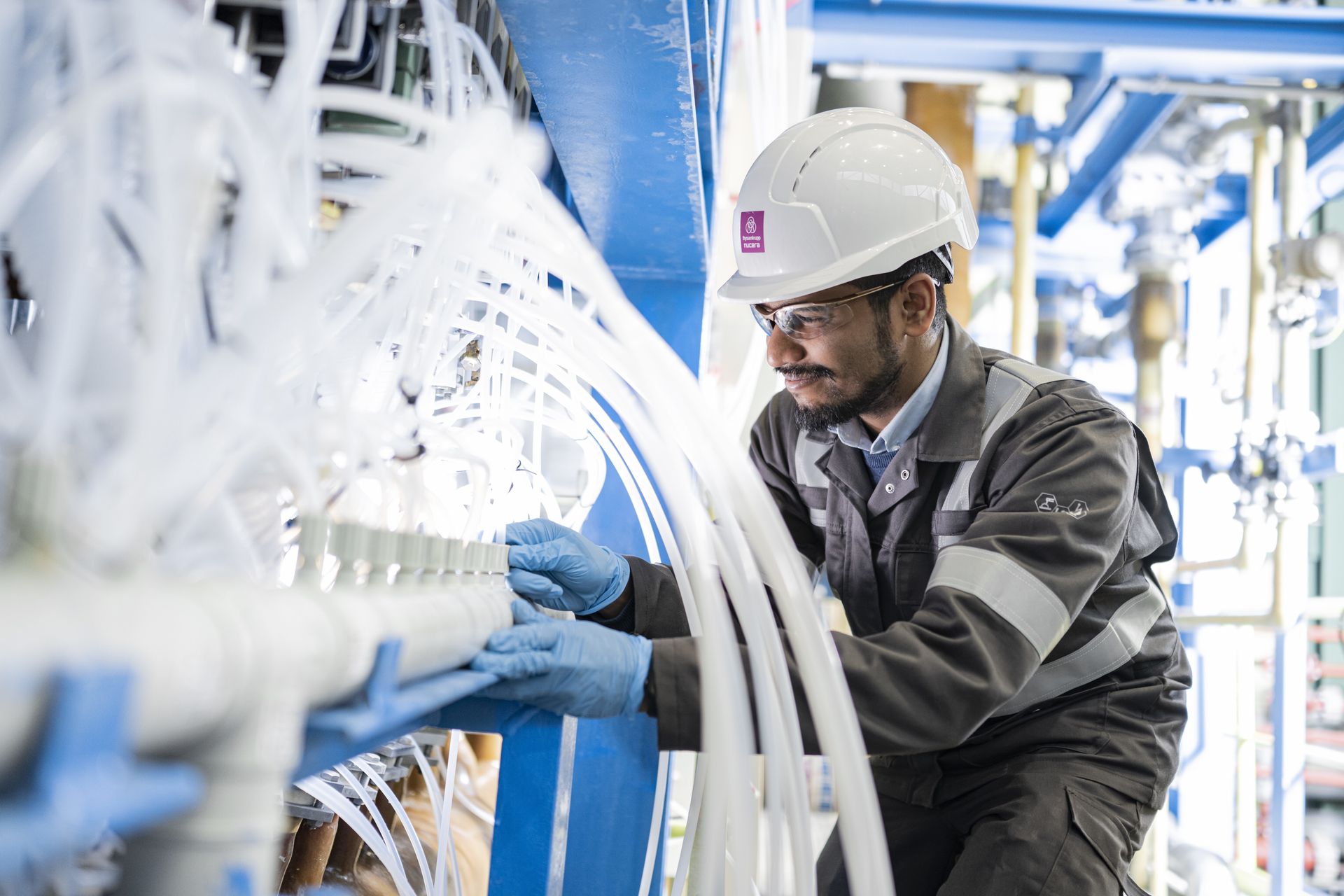 Ein Mitarbeiter prüft Leitungen und Komponenten einer industriellen Wasserelektrolyseanlage.
