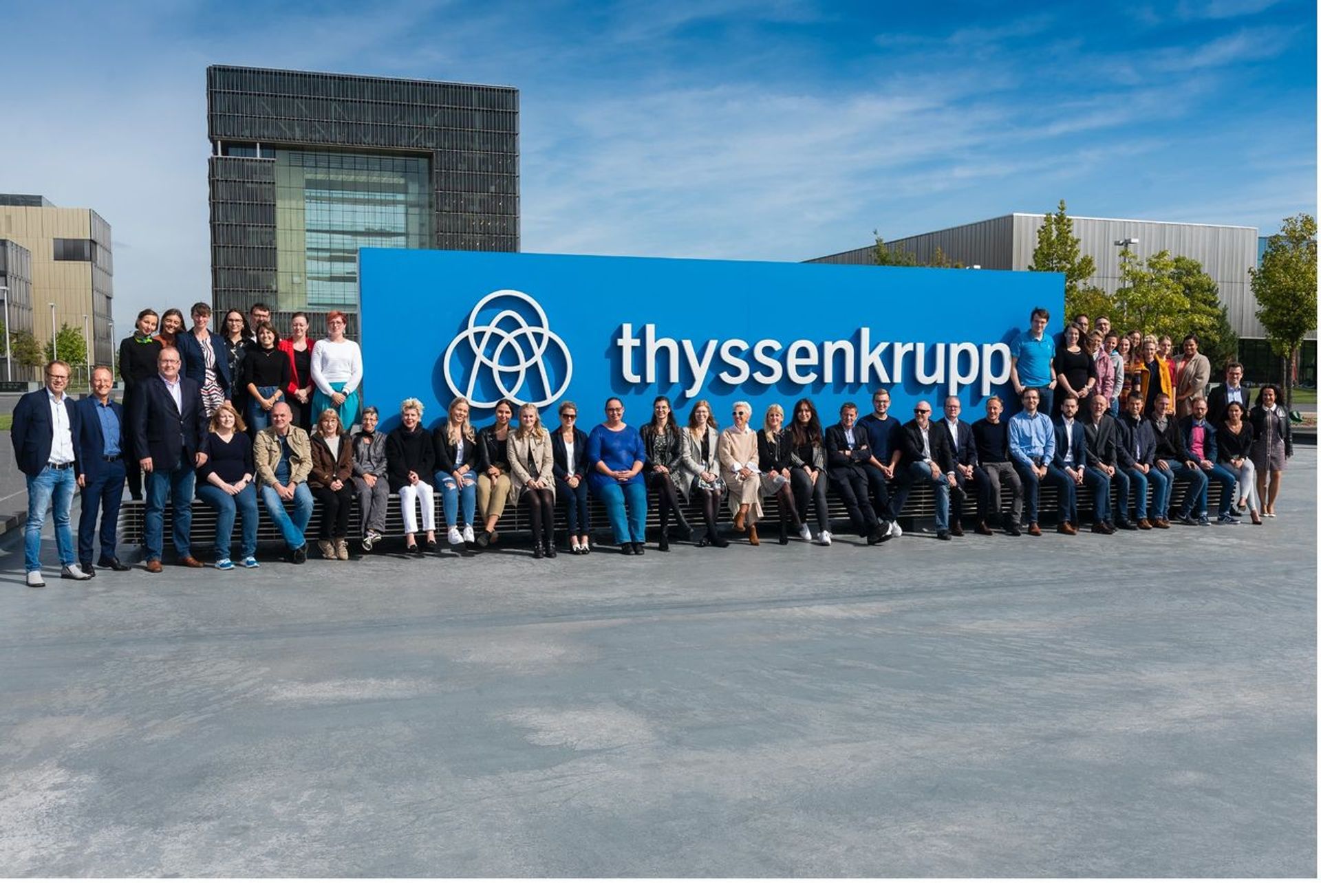 Team der Intellectual Property Abteilung von thyssenkrupp vor dem großen thyssenkrupp Logo am Unternehmensstandort