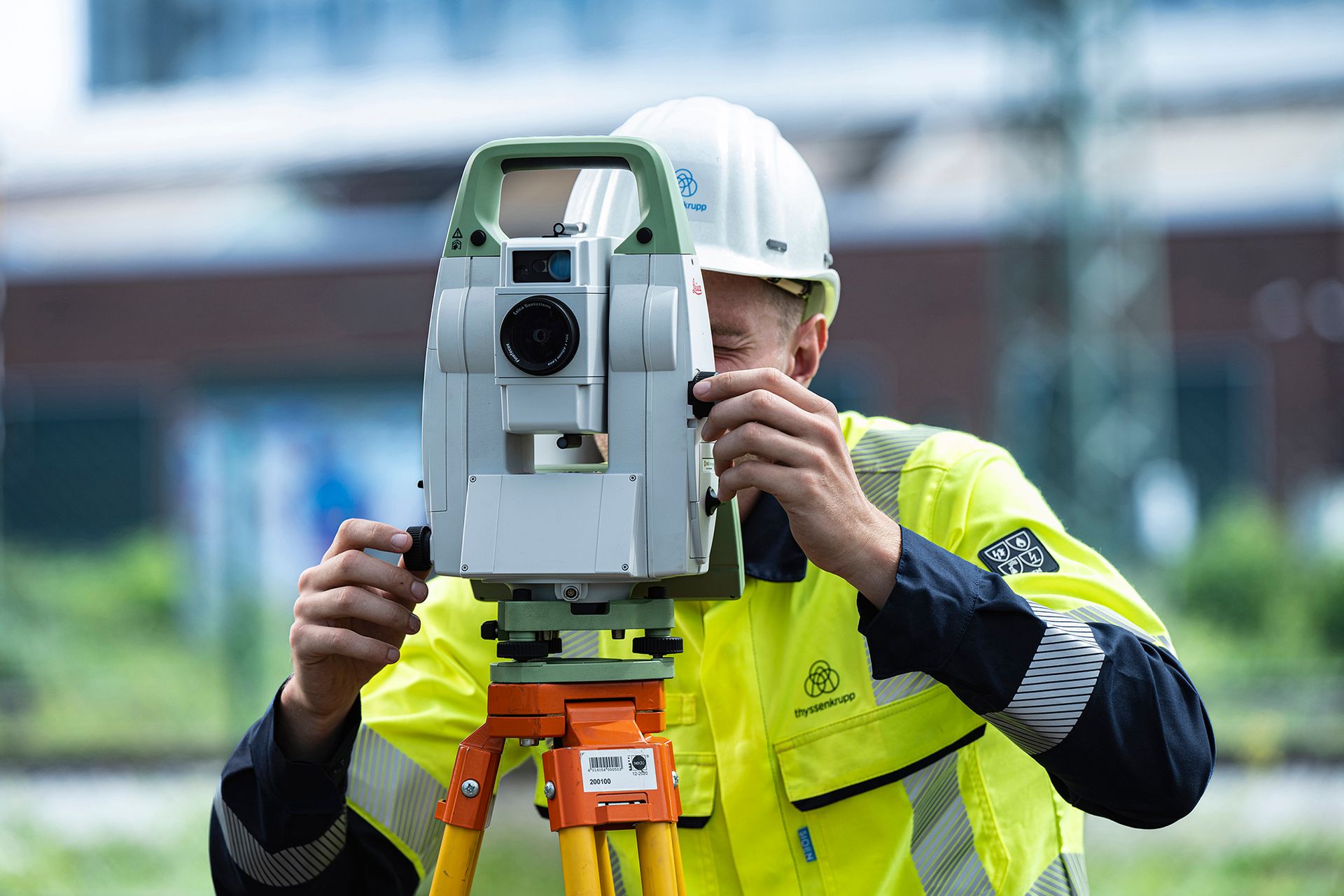 Person in Warnschutzkleidung bedient ein Vermessungsgerät auf einer Baustelle im Freien.