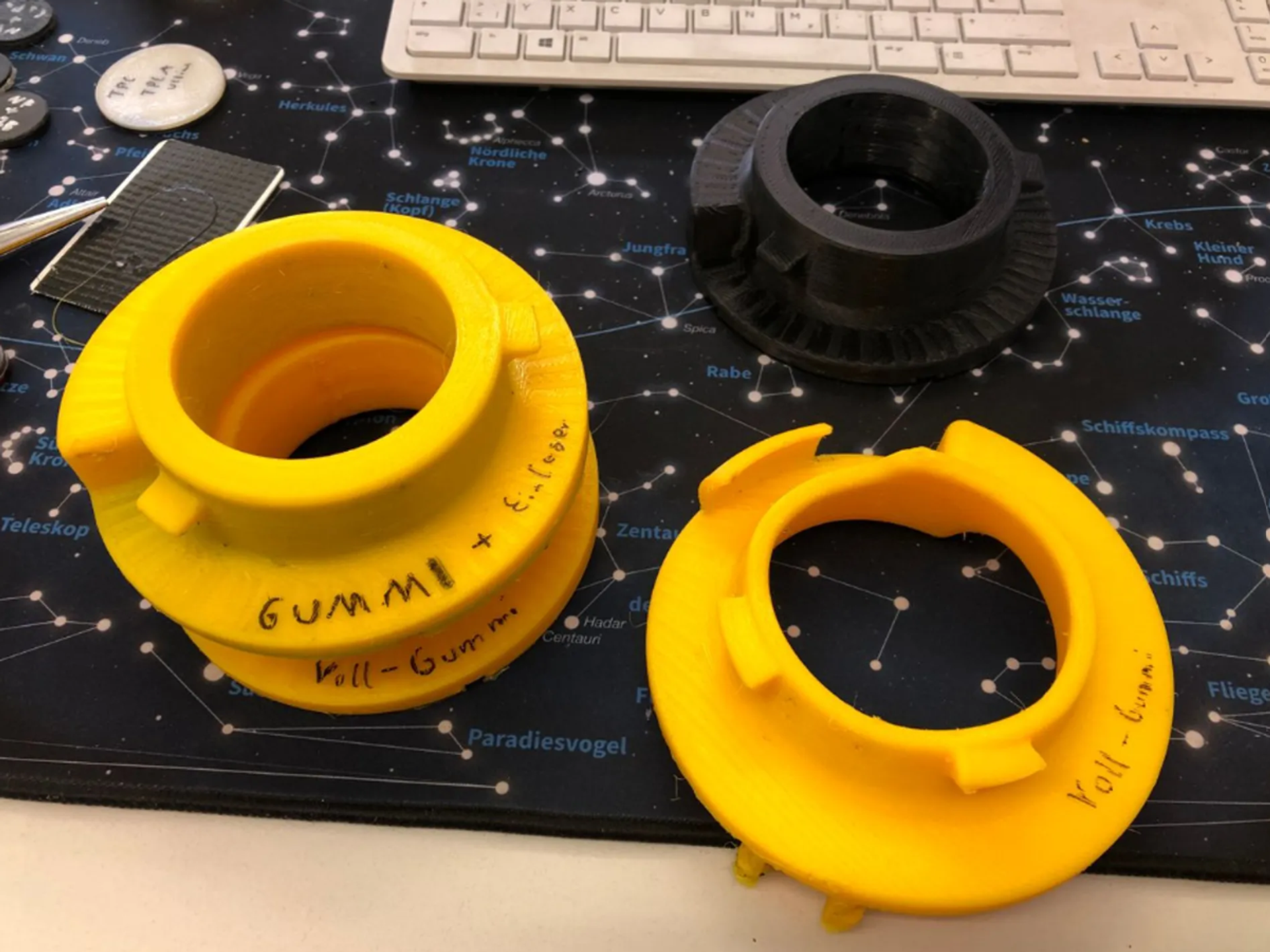 Drei gelbe und schwarze 3D-gedruckte Bauteile auf einem Schreibtisch.