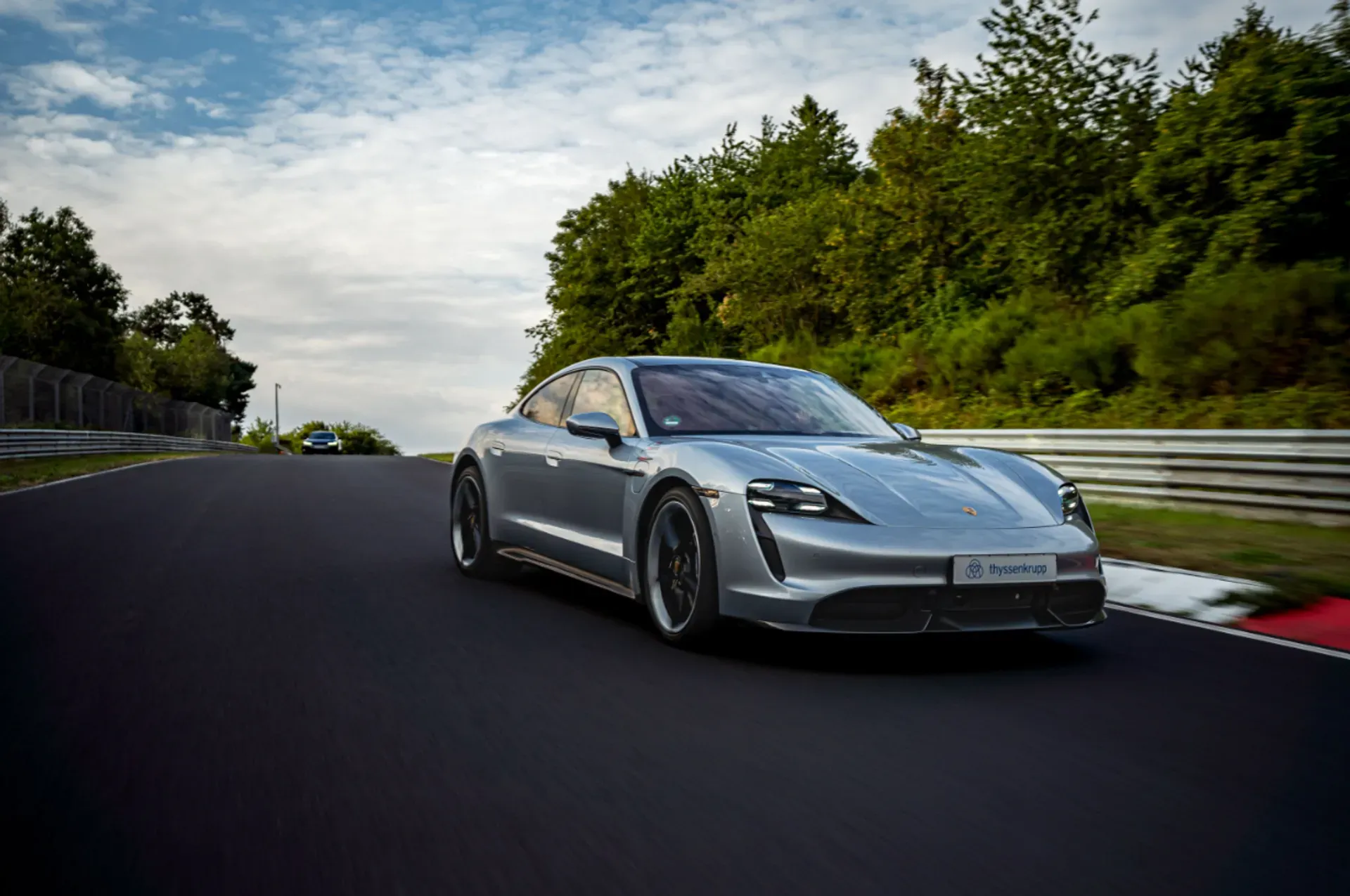 Ein graues Elektro-Sportfahrzeug fährt auf einer abgesperrten Teststrecke entlang von Leitplanken und Bäumen.