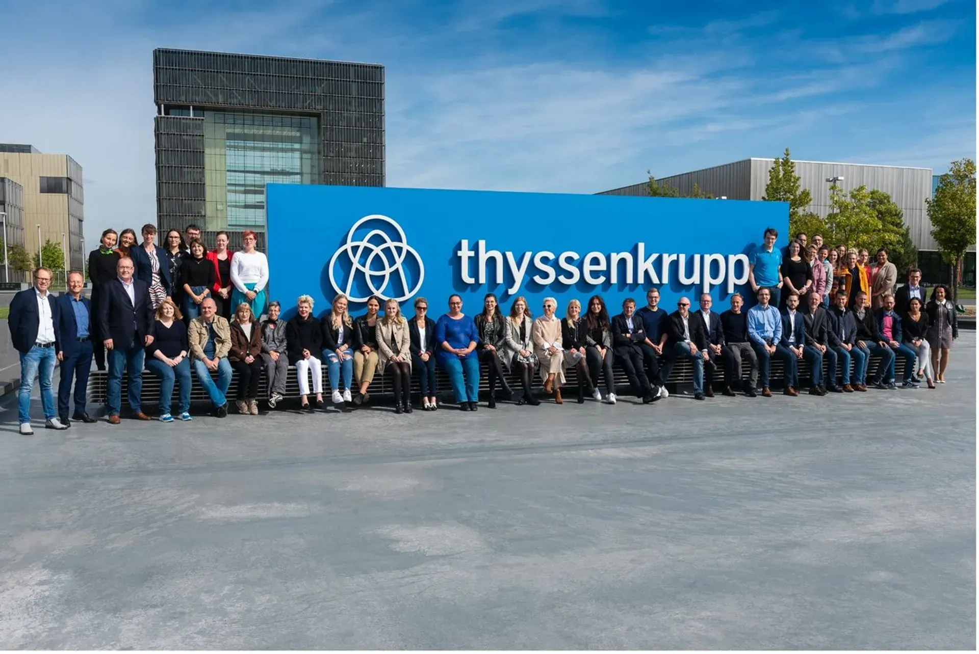 thyssenkrupp employees posing in front of company headquarters, representing teamwork and innovation in engineering and intellectual property.