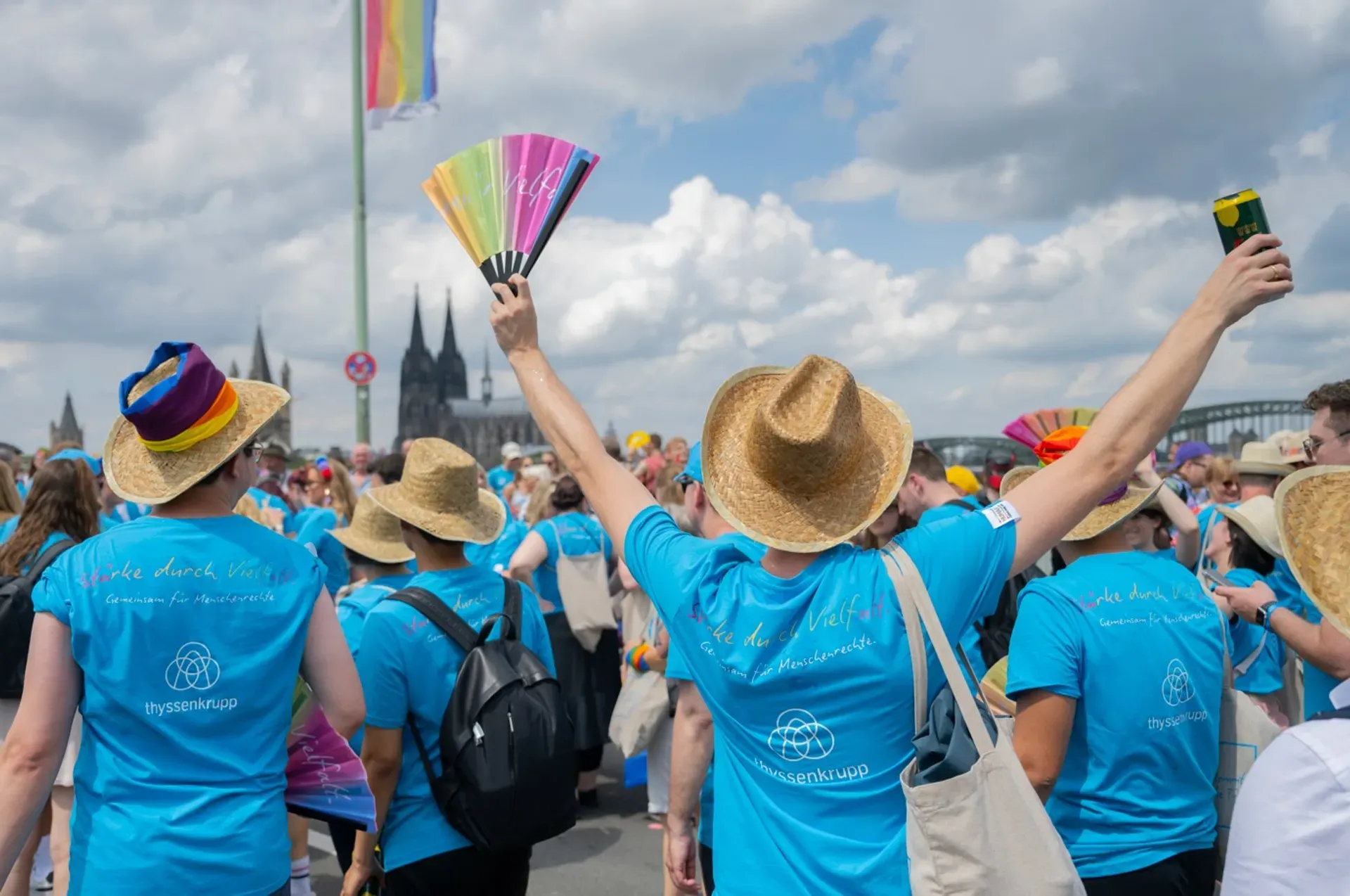 group of employees celebrating at a Pride parade, one person holding a colourful fan in the air surrounded by cheerful colleagues