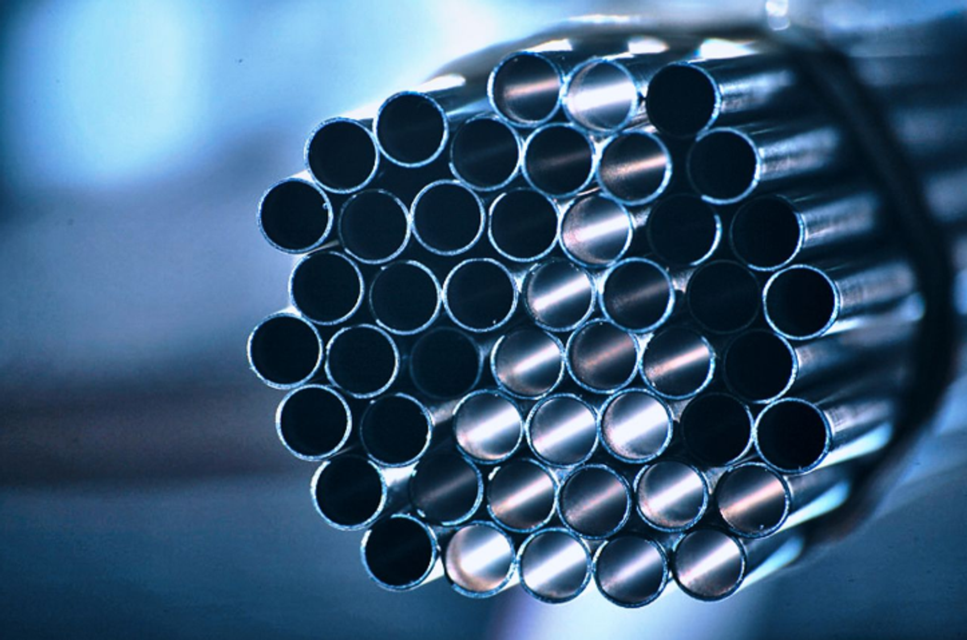 Bundle of many hollow metal tubes, closely grouped together and visible from the front, with a shiny surface against a blurred background.