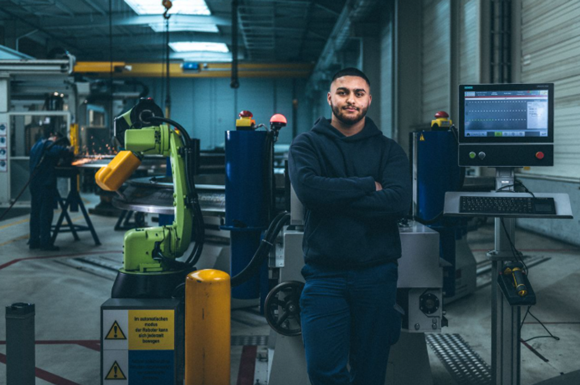 Mitarbeiter von thyssenkrupp arbeitet an einer automatisierten Fertigungsanlage mit Industrieroboter und digitaler Anlagensteuerung.