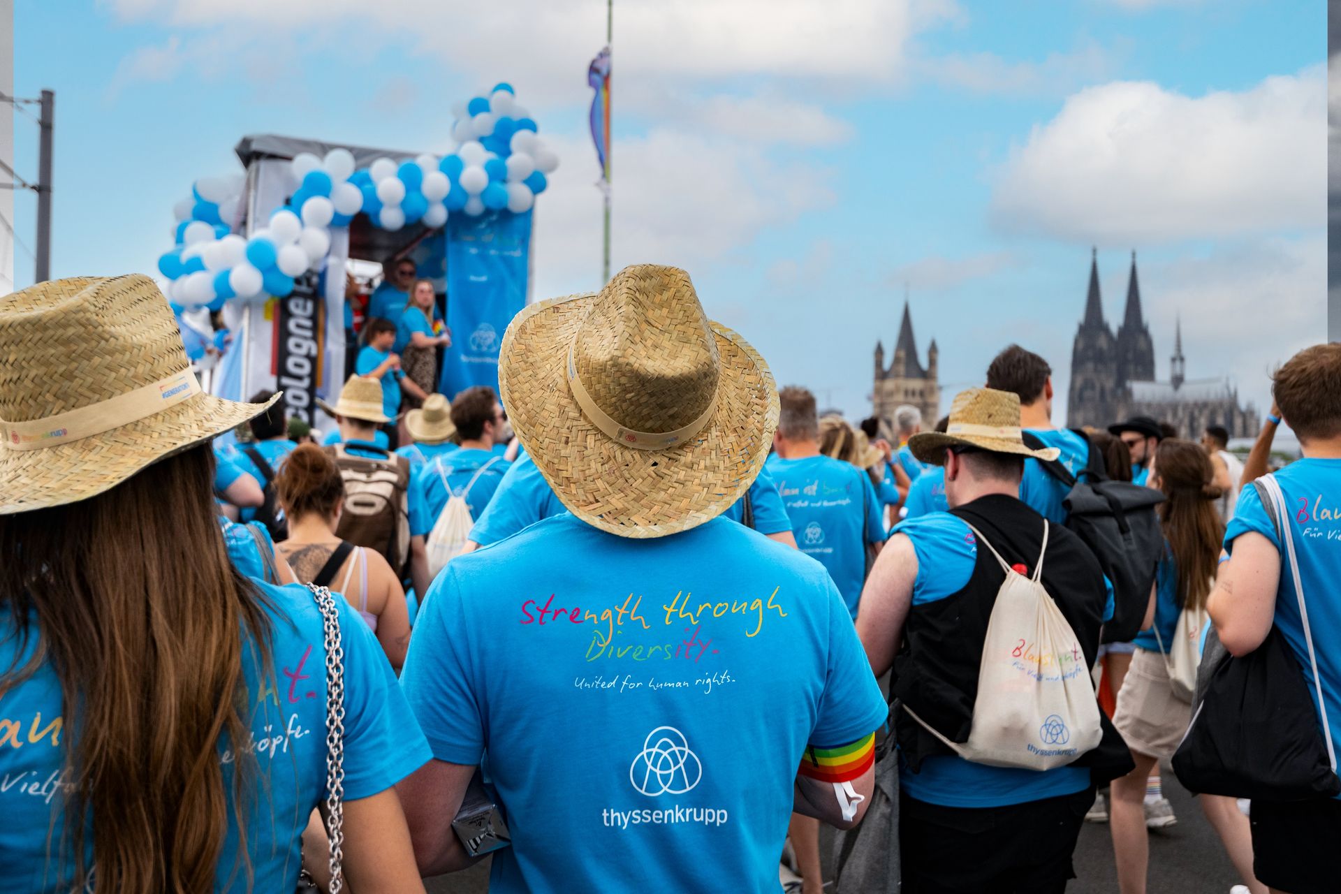 Participants of the Cologne Pride Parade wearing blue thyssenkrupp T-shirts with the slogan “Strength through diversity” in front of Cologne Cathedral.